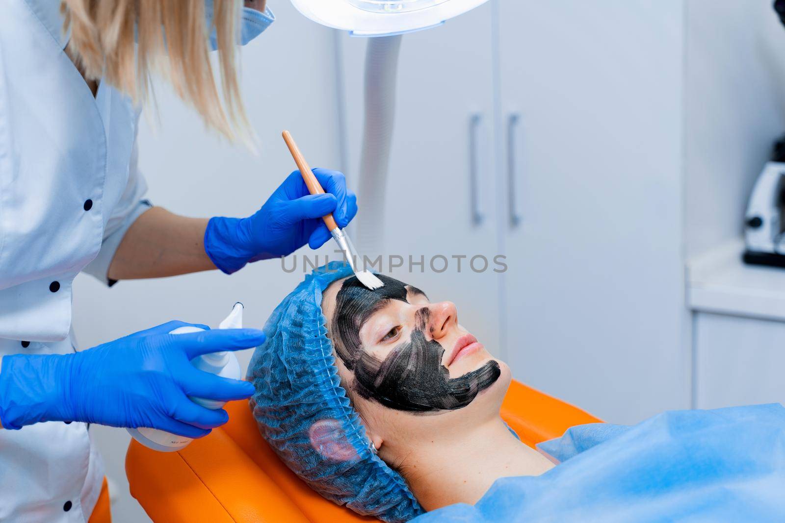 Dermatologist smears black mask on face for laser photorejuvenation and carbon peeling. Dermatology and cosmetology. Using surgical laser by Rabizo