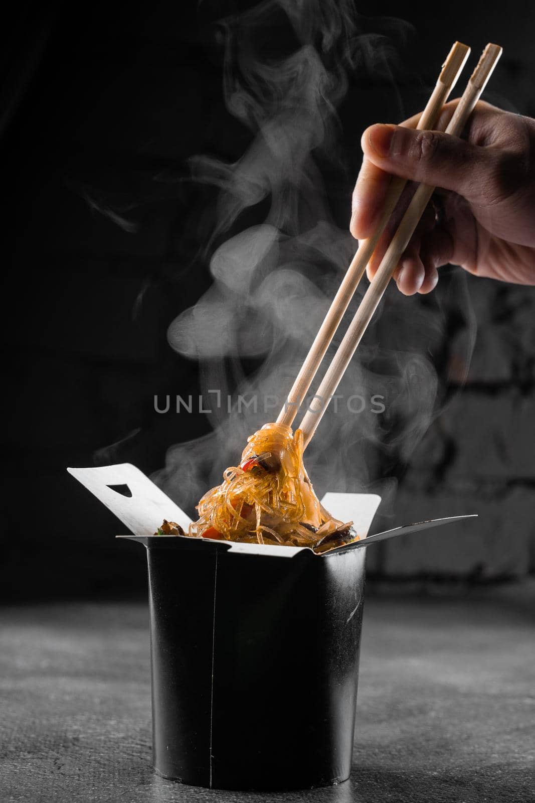 Steaming rice noodles in wok box on black background. Fast food delivery service. Takeaway chinese street meal. Udon in black food container. by Rabizo