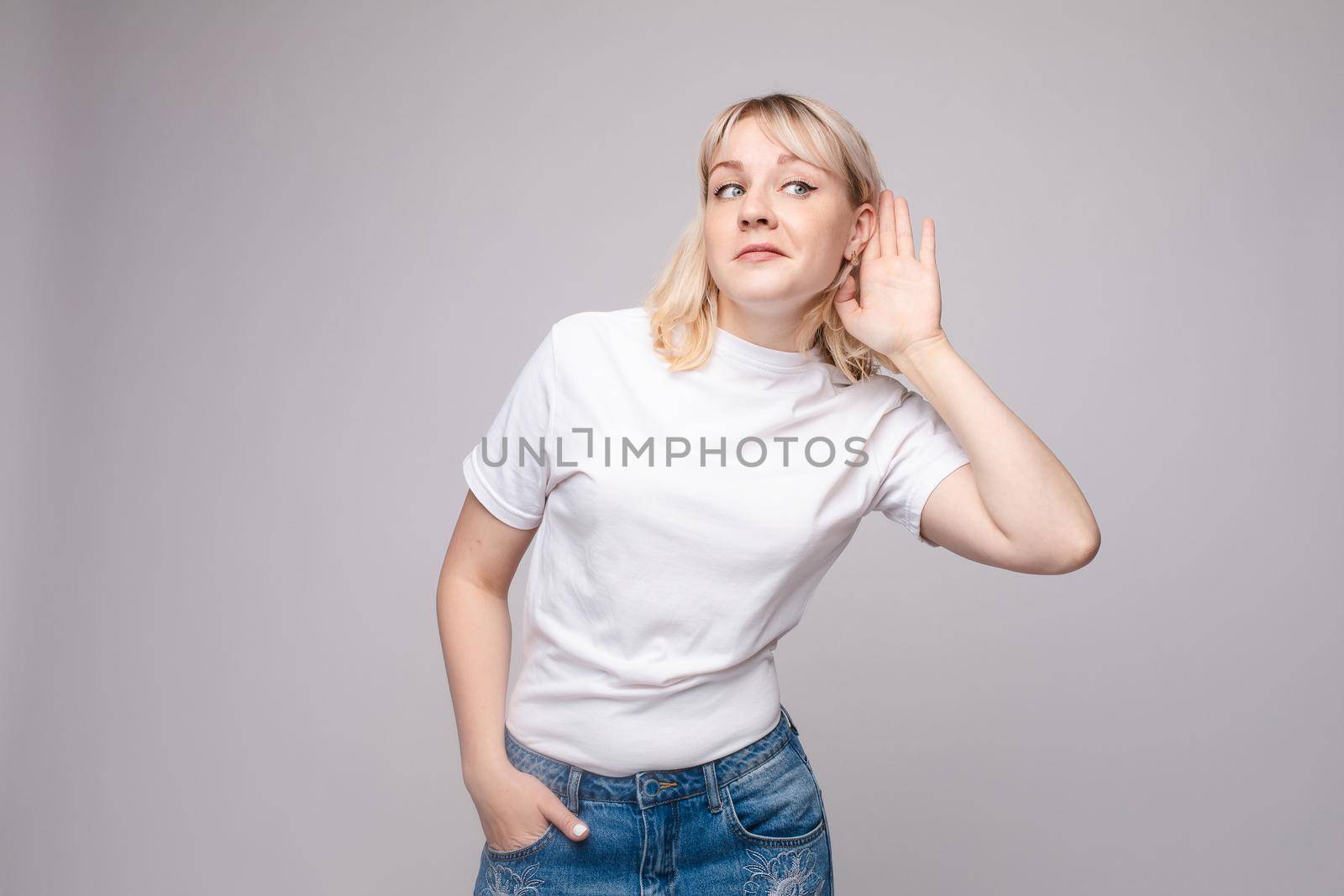 Studio portrait of curious brunette girl in multicolored top listening to the news or gossips with her ear.