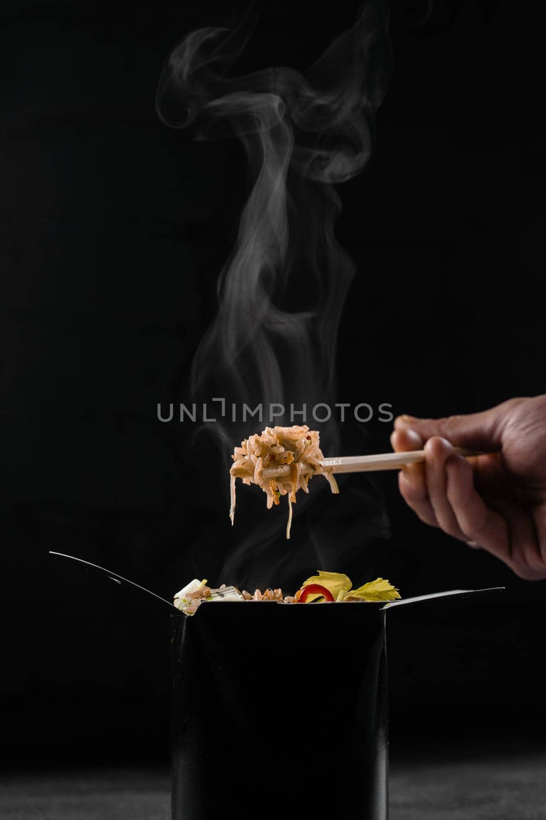 Steaming hot rice in wok box on black background. Holding rice with chinese chopsticks. Asian spicy dish for street restaurant and fast food delivery service. by Rabizo