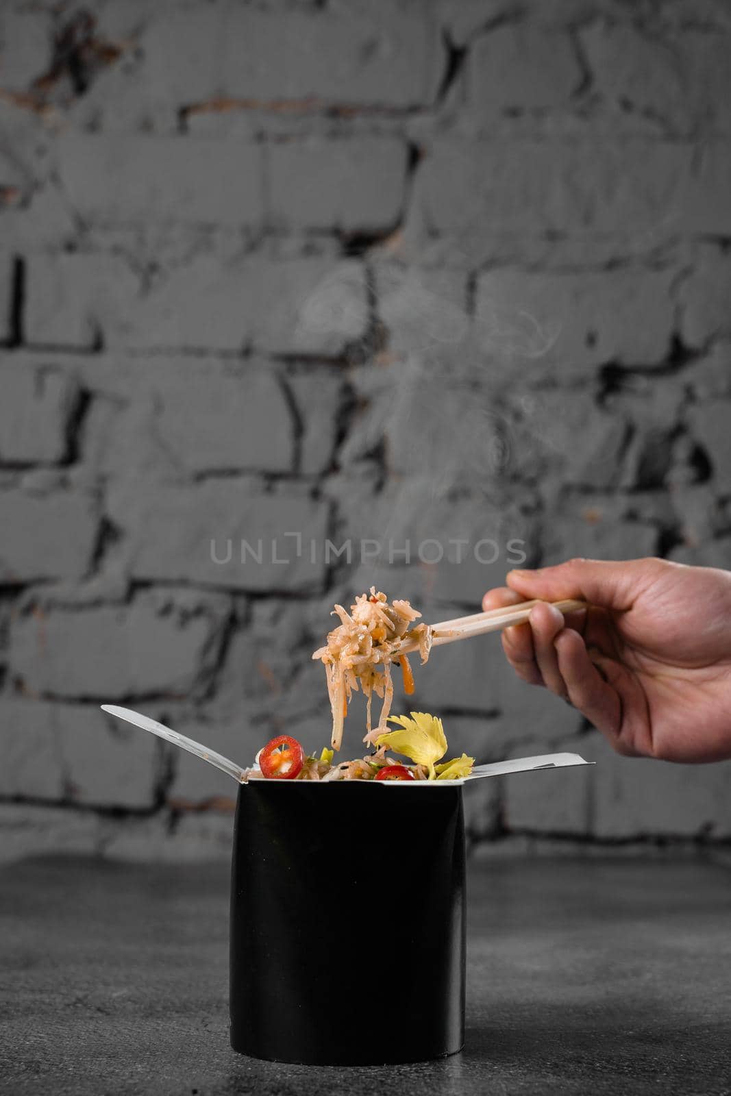 Steaming hot rice in wok box on black background. Holding rice with chinese chopsticks. Asian spicy dish for street restaurant and fast food delivery service