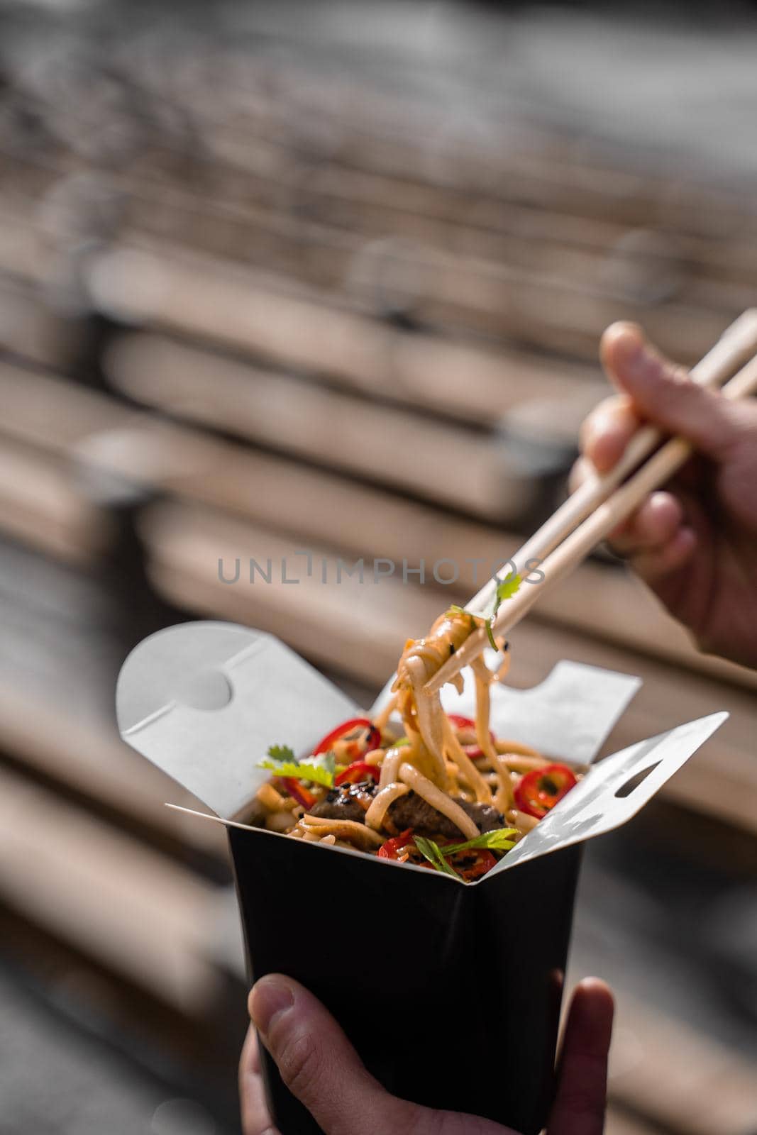 Wok in box in black food container. Holding spicy noodles with chopsticks. Fast food delivery service. Takeaway chinese street meal. by Rabizo