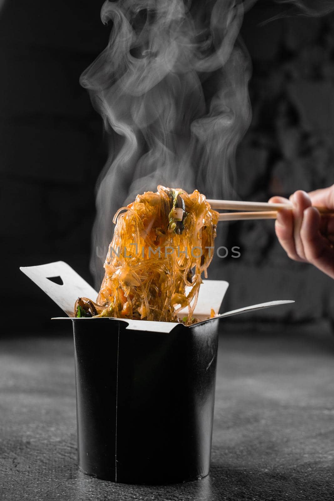 Steaming rice noodles in wok box on black background. Fast food delivery service. Takeaway chinese street meal. Udon in black food container. by Rabizo