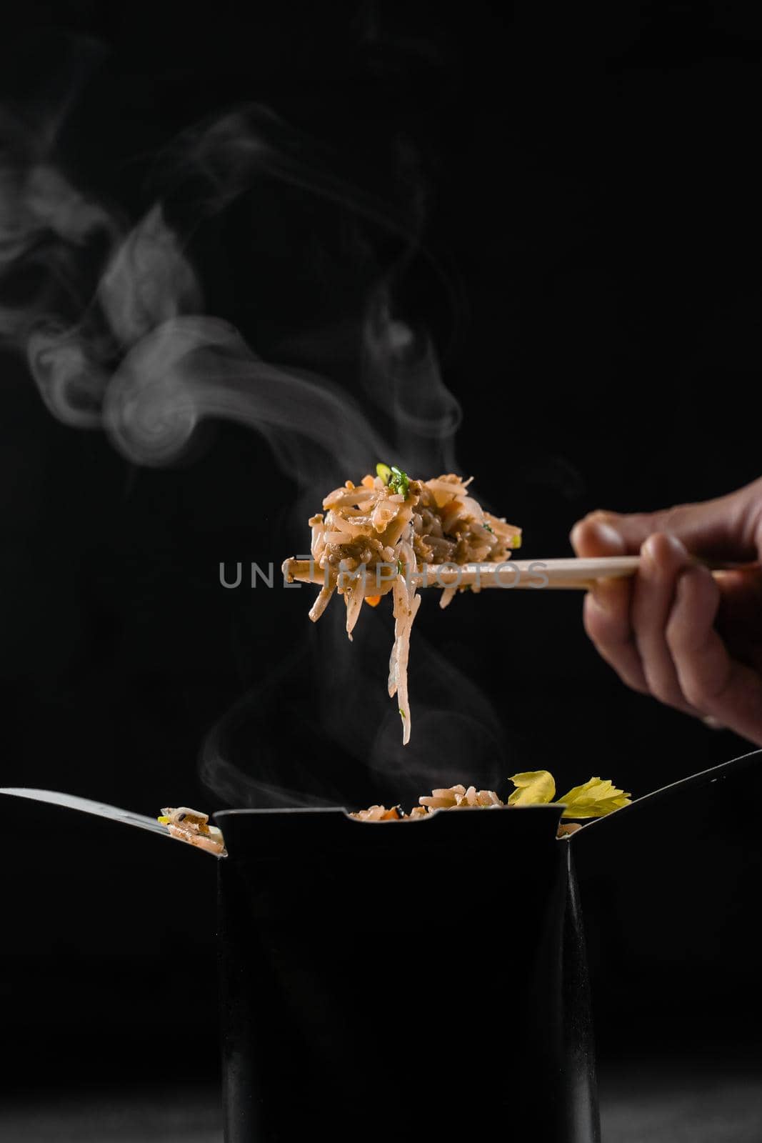 Steaming hot rice in wok box on black background. Holding rice with chinese chopsticks. Asian spicy dish for street restaurant and fast food delivery service. by Rabizo