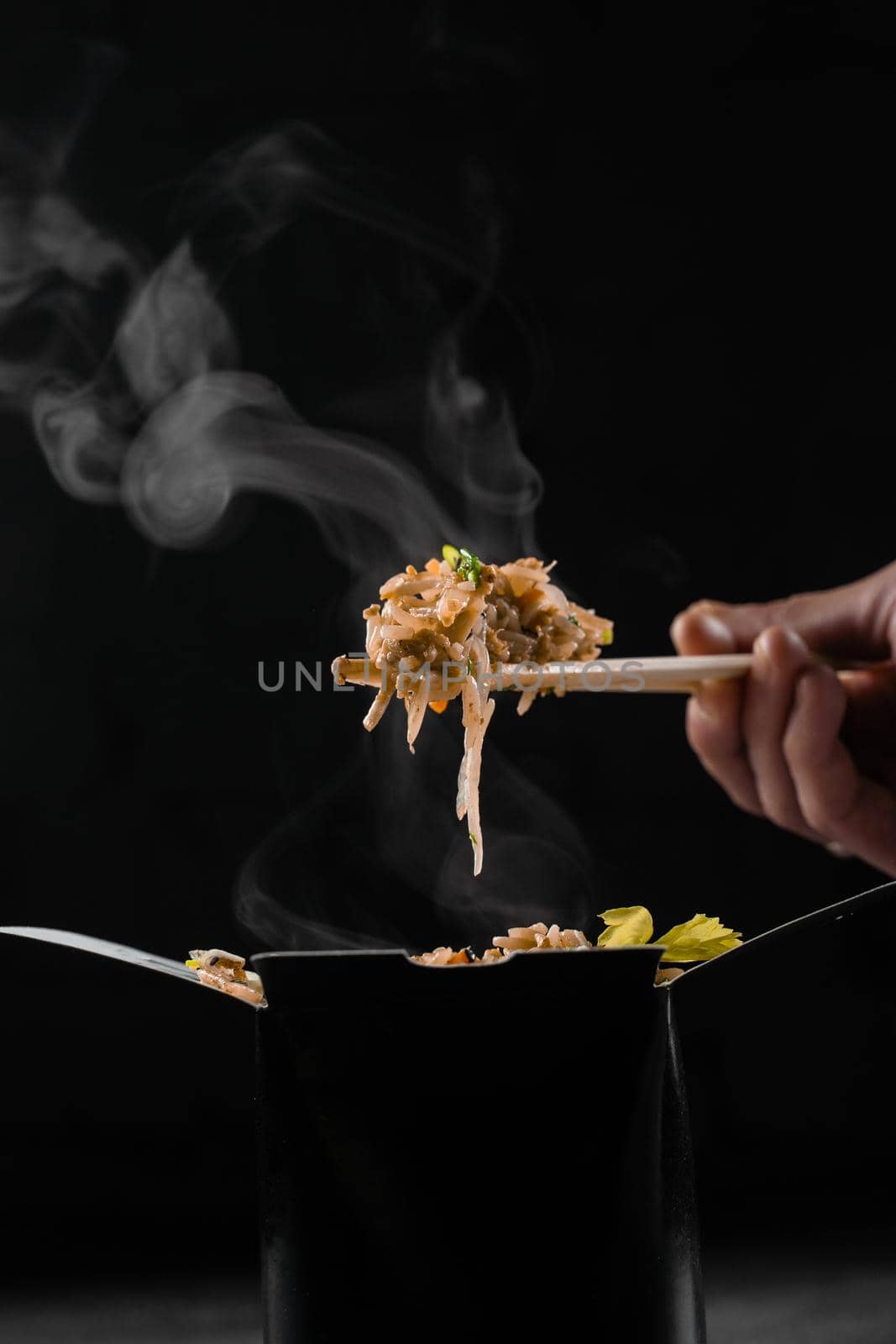 Steaming hot rice in wok box on black background. Holding rice with chinese chopsticks. Asian spicy dish for street restaurant and fast food delivery service