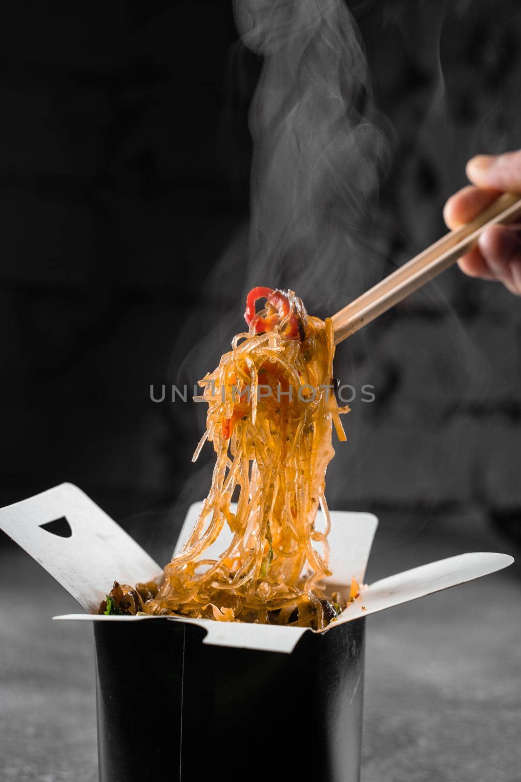 Steaming rice noodles in wok box on black background. Fast food delivery service. Takeaway chinese street meal. Udon in black food container. by Rabizo