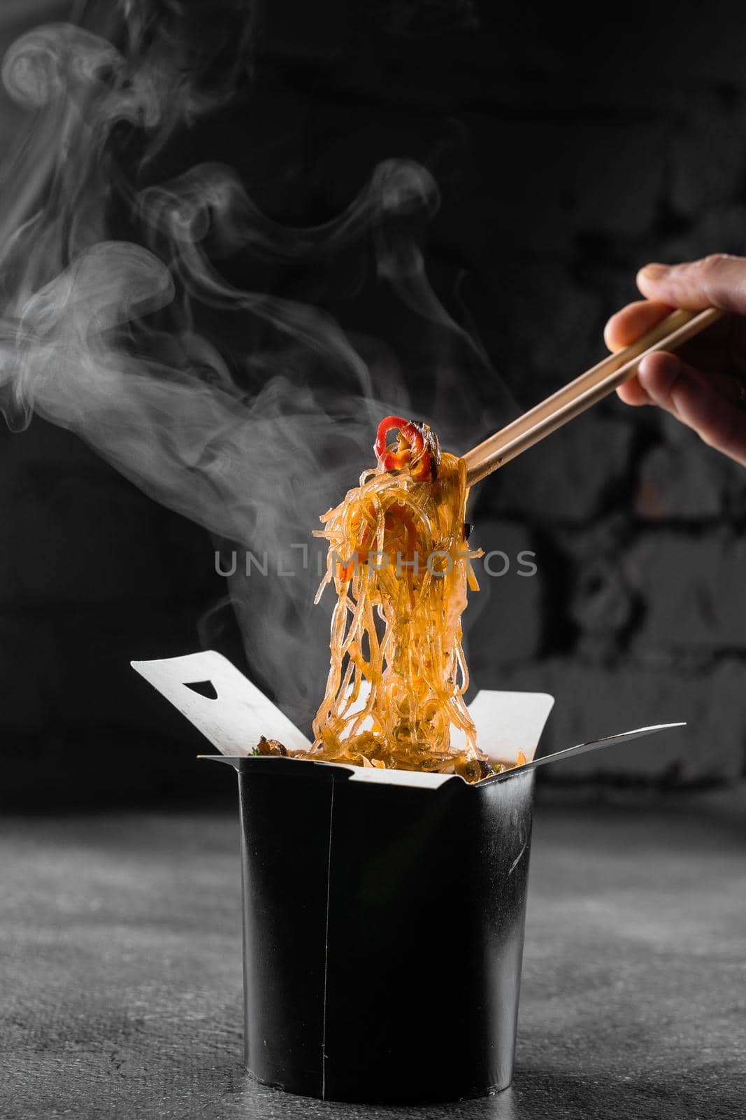 Steaming rice noodles in wok box on black background. Fast food delivery service. Takeaway chinese street meal. Udon in black food container