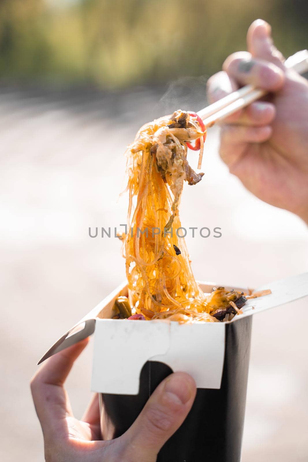 Wok in box in black food container. Holding rice noodles with chopsticks. Fast food delivery service. Takeaway chinese street meal. Eating udon.