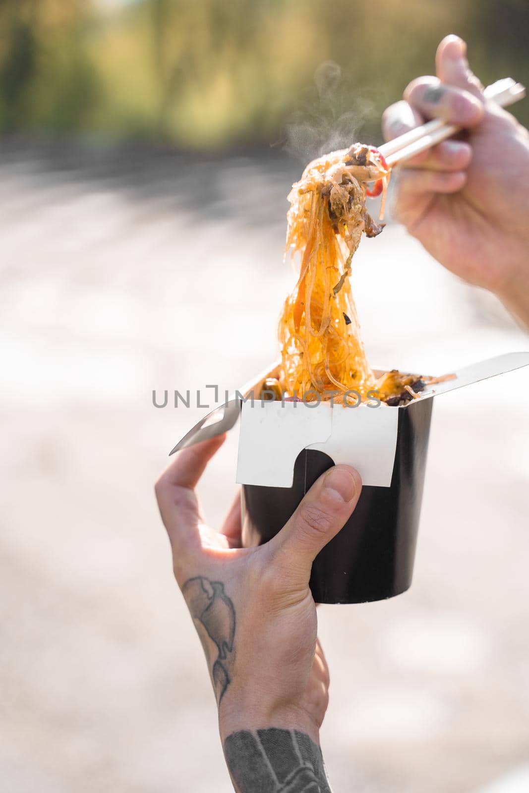 Wok in box in black food container. Holding rice noodles with chopsticks. Fast food delivery service. Takeaway chinese street meal. Eating udon.