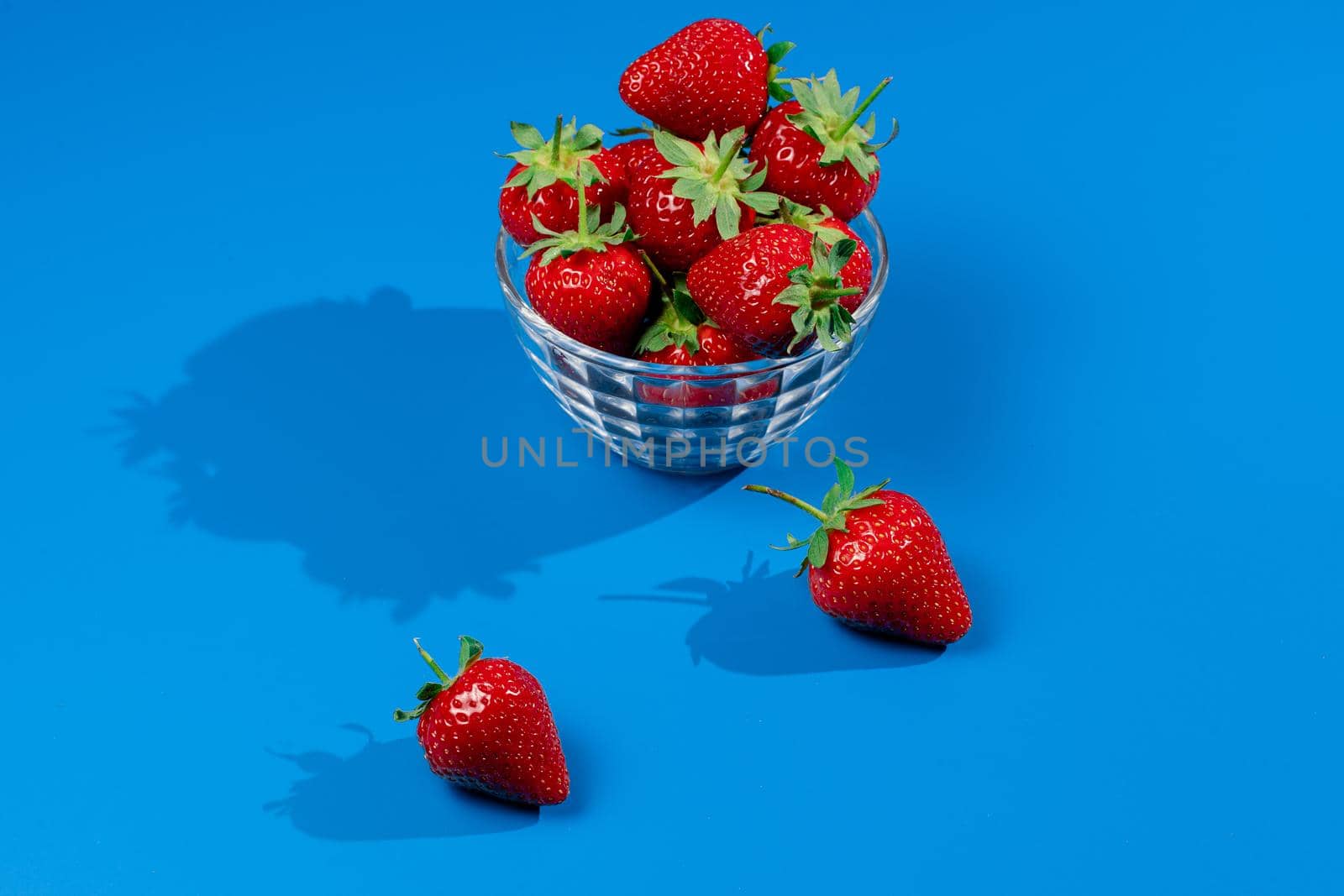 Bunch of strawberry in bowl on blue background. Yummy summer fruit