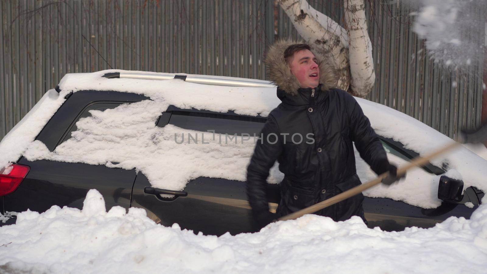 A young man in a jacket digs his car out of a snowdrift with a shovel. The car was covered in snow. Weather disaster. 4k