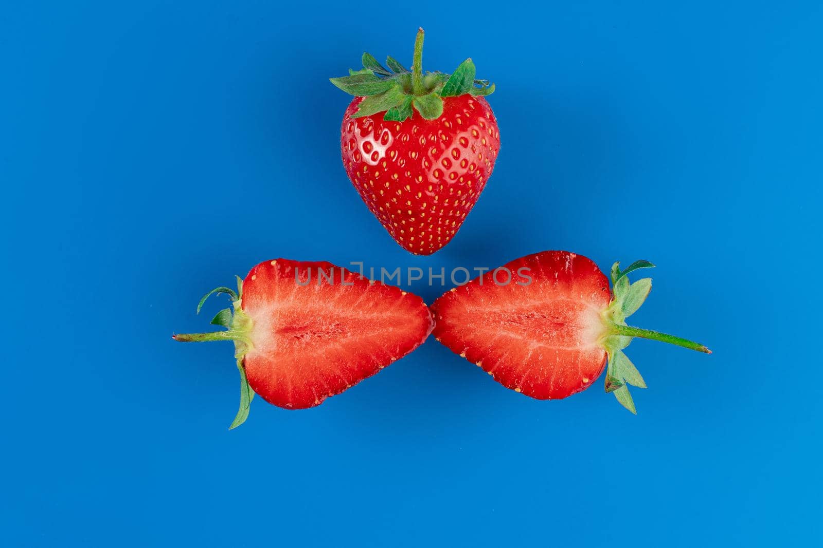 Strawberry slices close-up and full piece of strawberries on blue background. Seasonal berry.