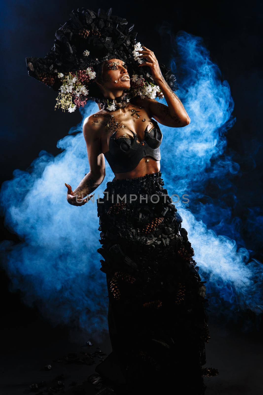 Portrait of a model in a headdress and dress made of coal. There is blue smoke behind the model.