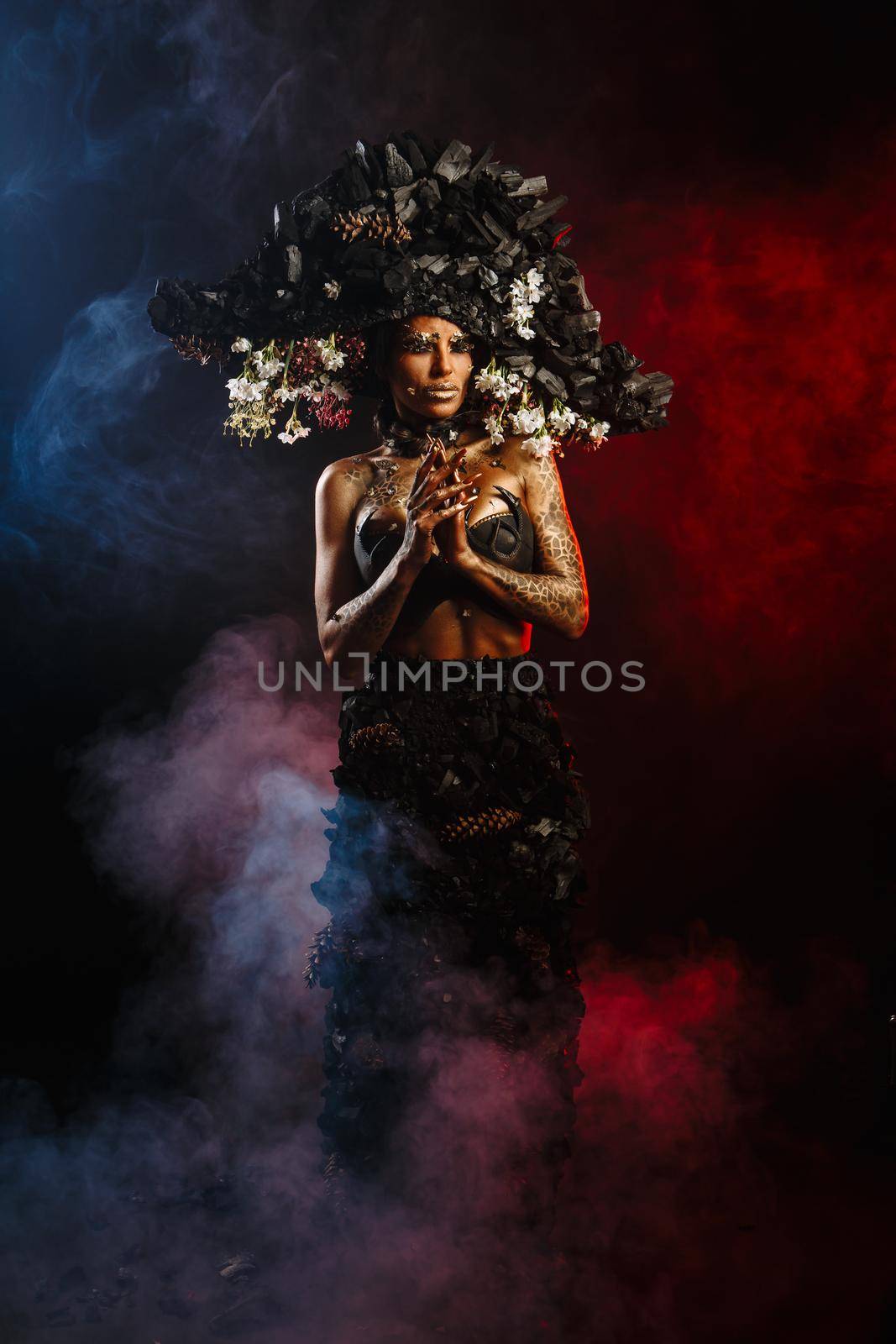 Portrait of a model in a headdress and dress made of coal. There is red smoke behind the model.
