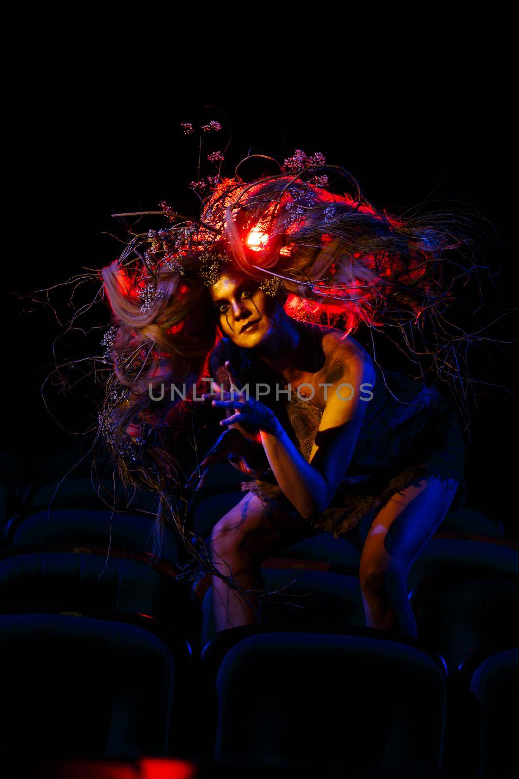 The girl who plays the role of a Ghost or spirit in the theater is sitting between the rows of chairs by deandy