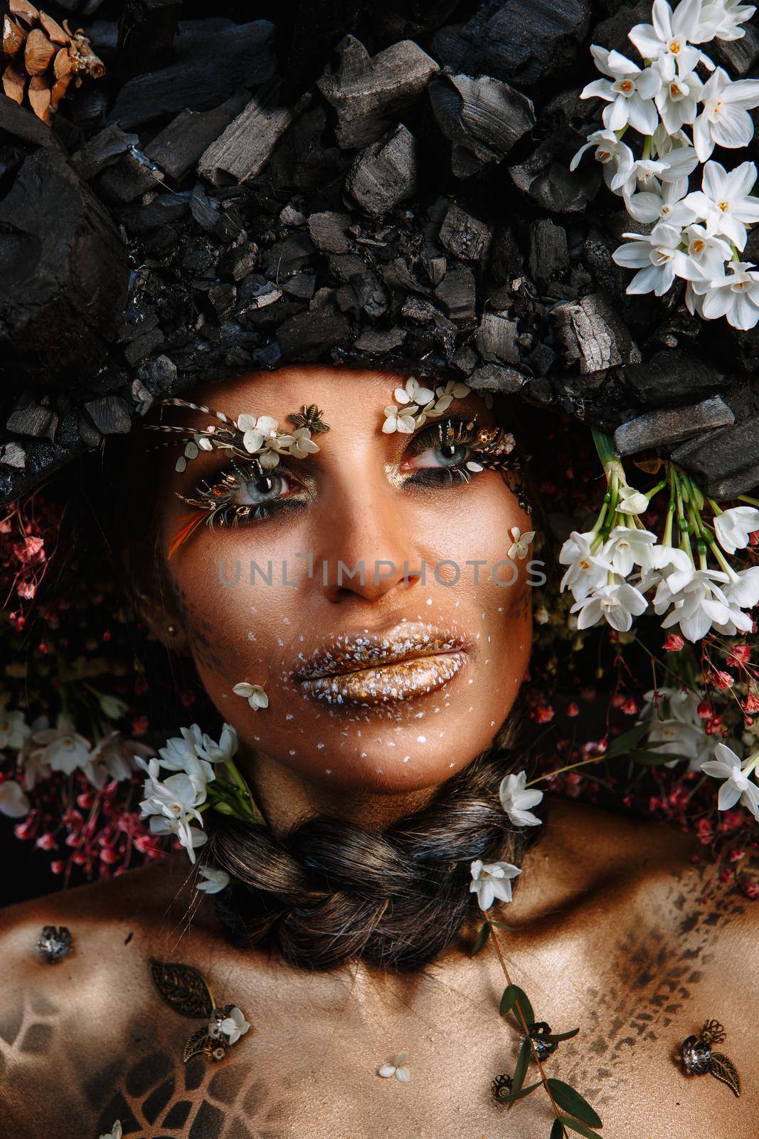 A large portrait of a model in a headdress made of coal. Bright makeup and body.