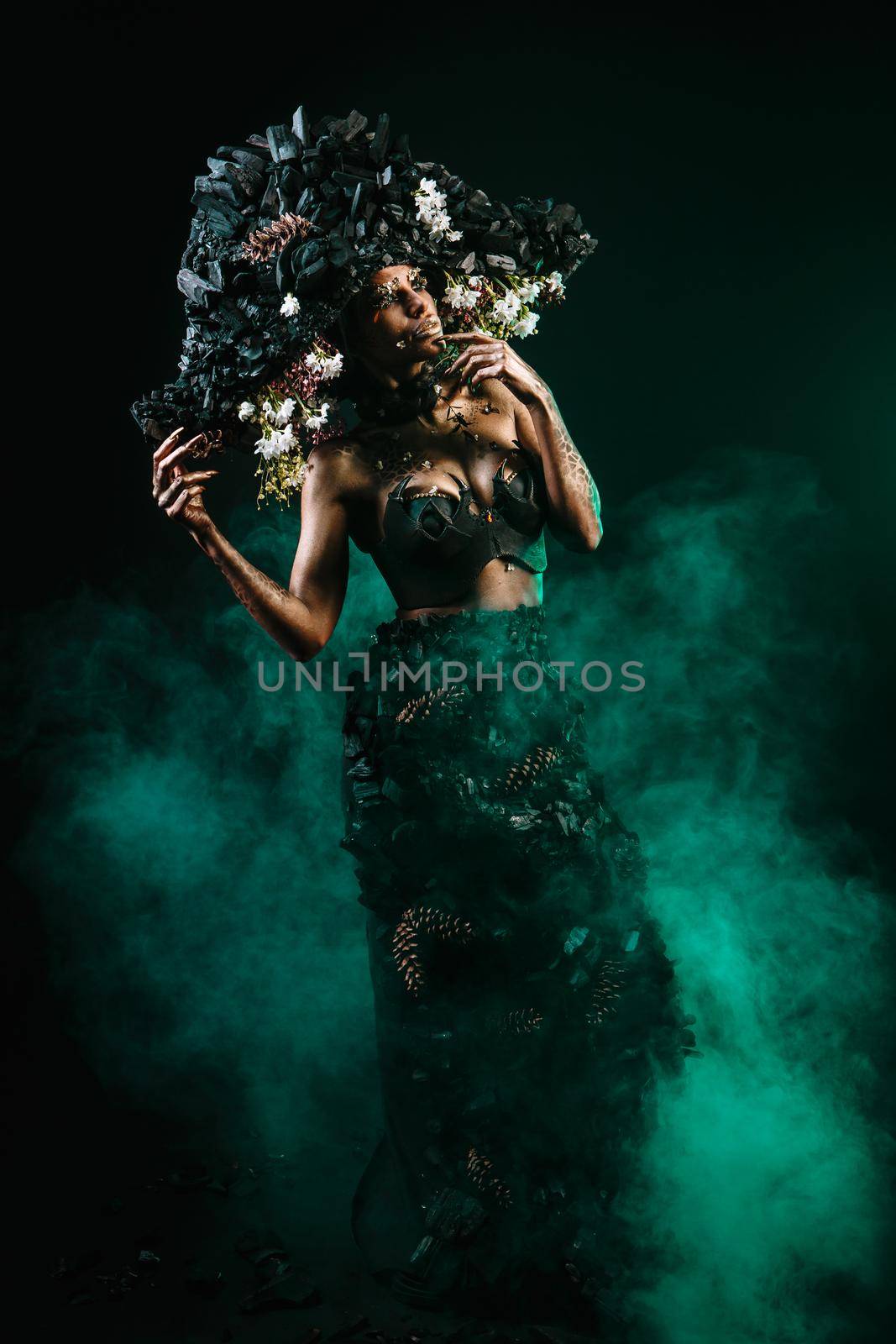 Portrait of a model in a headdress and dress made of coal. There is green smoke behind the model.