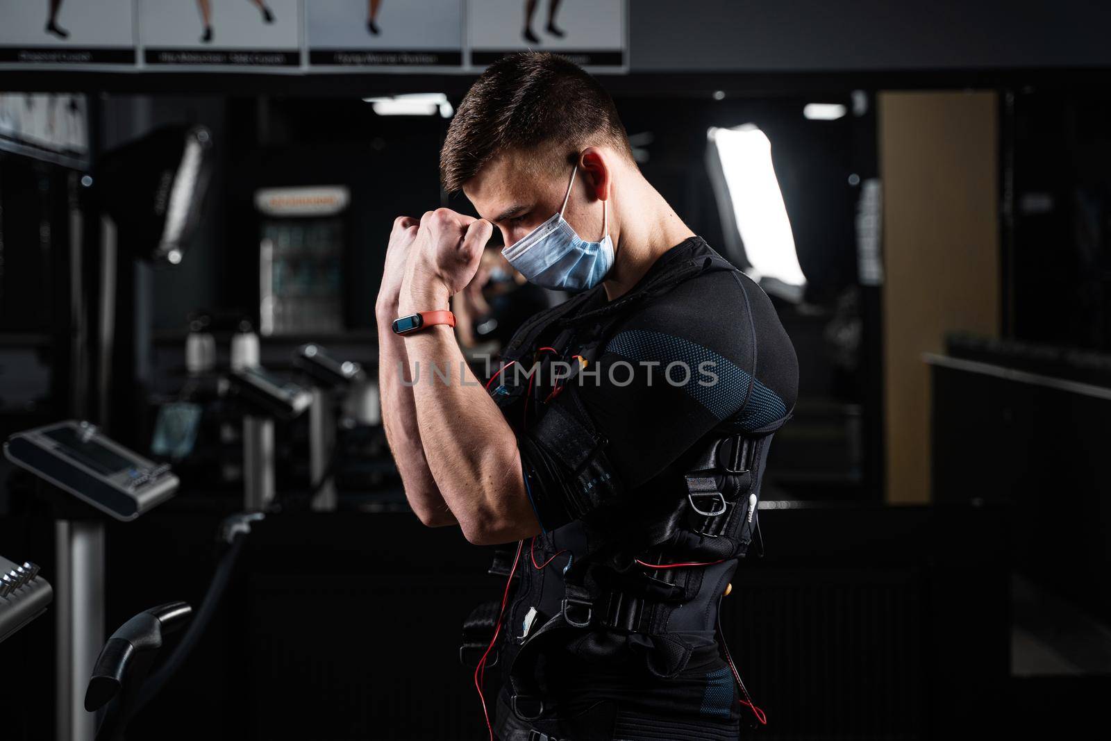 Man in EMS suit and medical mask in gym. Protection from coronavirus covid-19. Sport training in electrical muscle stimulation suit at quarantine period