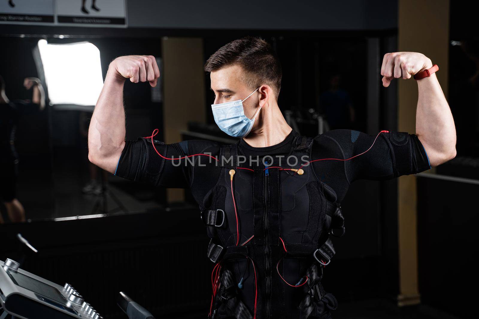 Man in EMS suit and medical mask in gym. Protection from coronavirus covid-19. Sport training in electrical muscle stimulation suit at quarantine period