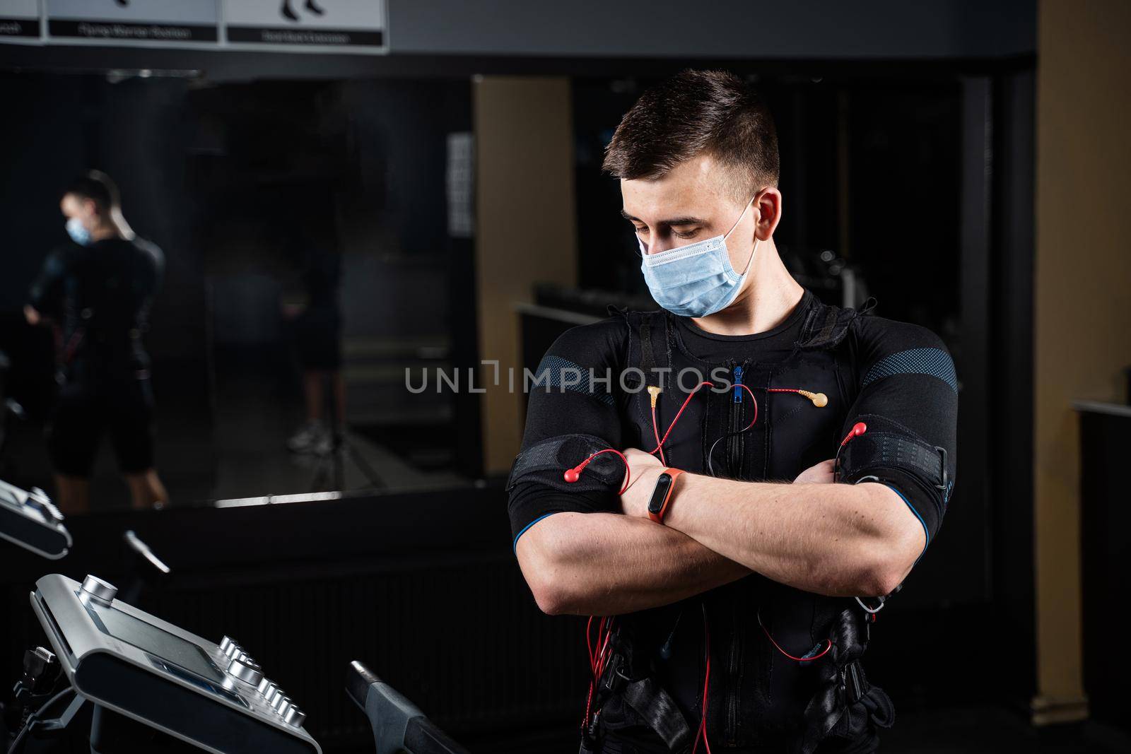 Man in EMS suit and medical mask in gym. Protection from coronavirus covid-19. Sport training in electrical muscle stimulation suit at quarantine period. by Rabizo