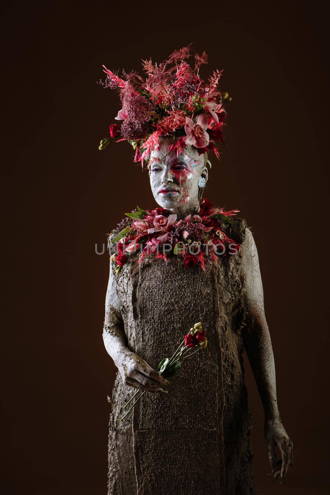 A girl smeared with clay. The model has a headdress made of flowers.