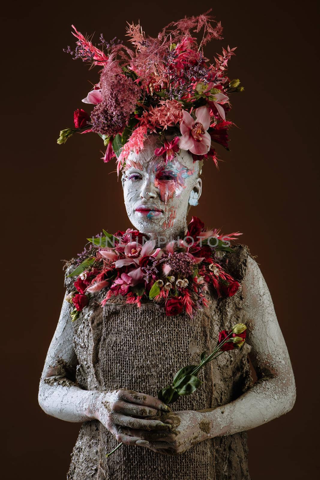 A girl smeared with clay. The model has a headdress made of flowers.