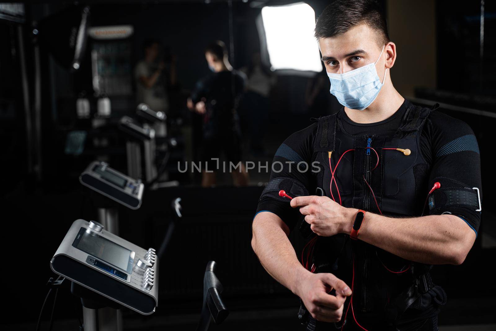 Man in EMS suit and medical mask in gym. Protection from coronavirus covid-19. Sport training in electrical muscle stimulation suit at quarantine period