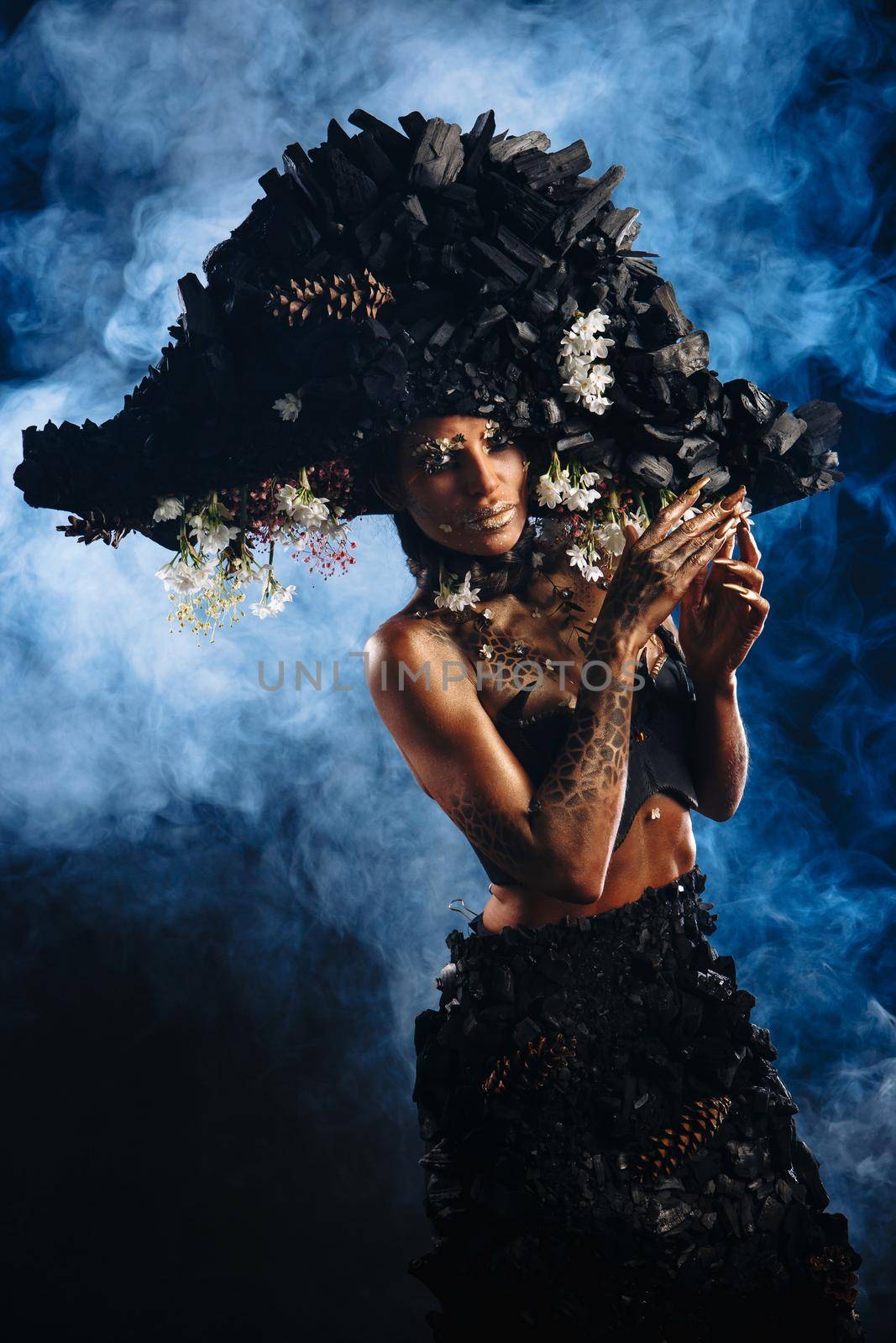 Portrait of a model in a headdress and dress made of coal. There is blue smoke behind the model.