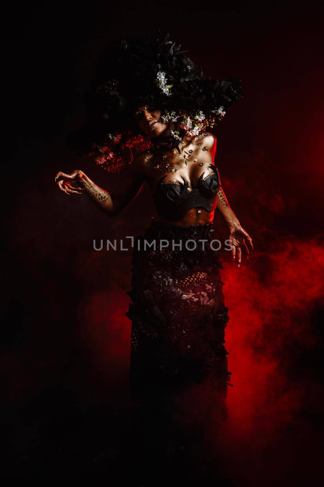 Portrait of a model in a headdress and dress made of coal. There is red smoke behind the model.