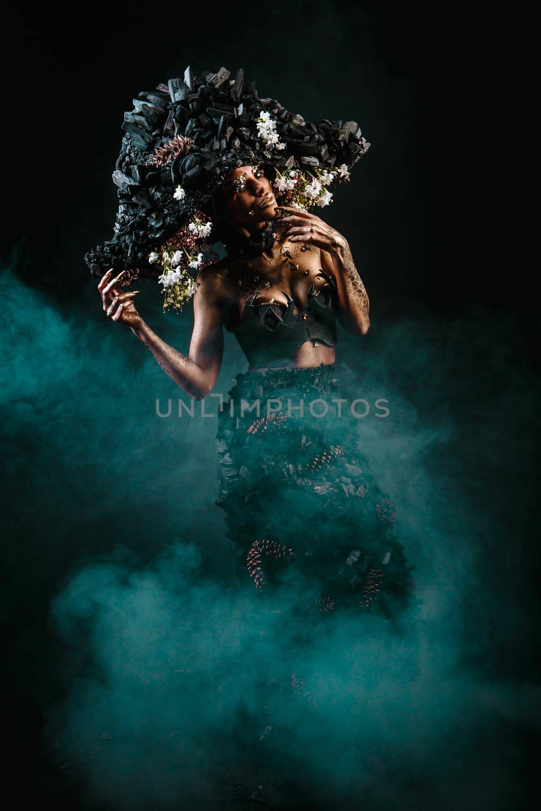 Portrait of a model in a headdress and dress made of coal. There is green smoke behind the model.