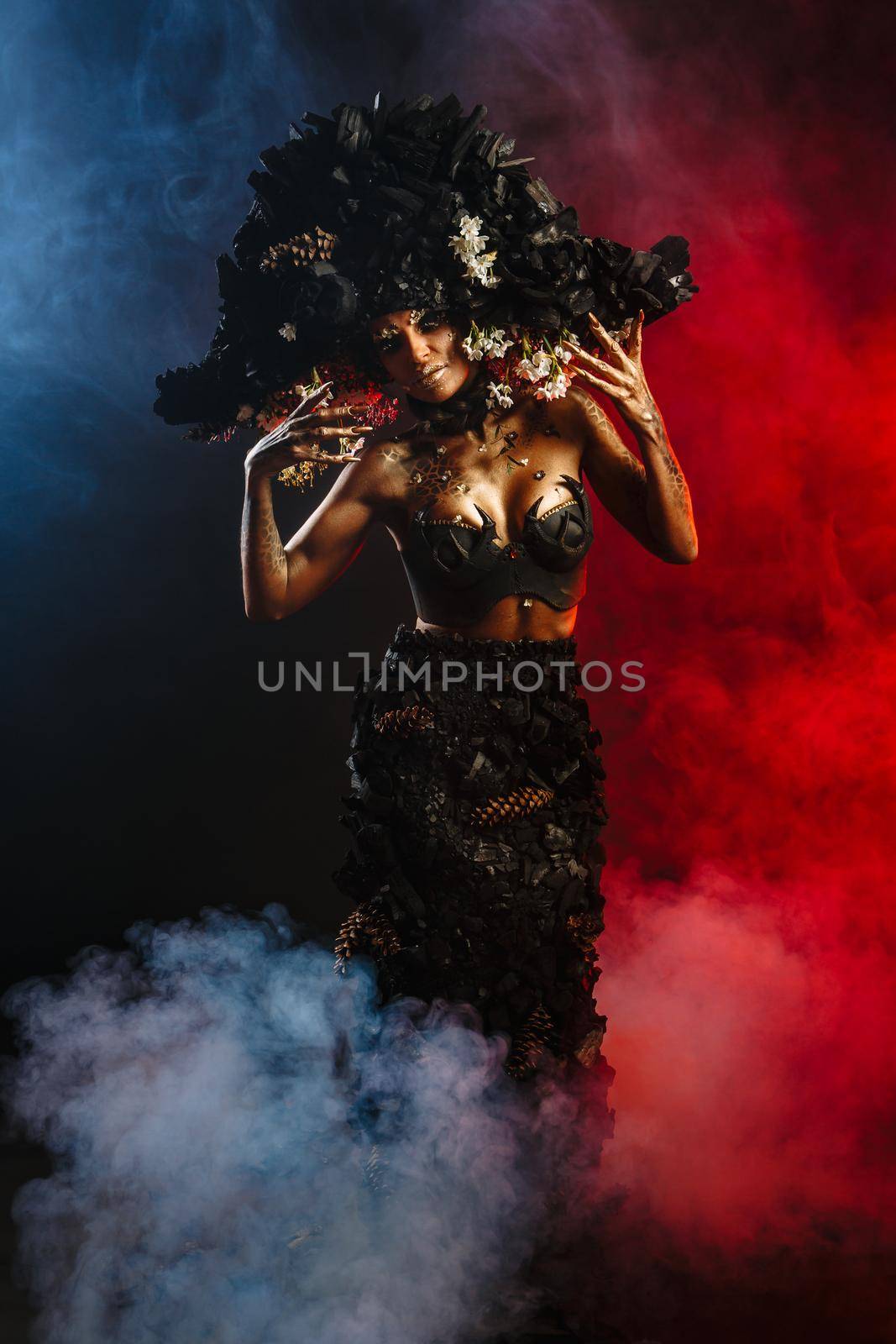 Portrait of a model in a headdress and dress made of coal. There is red smoke behind the model by deandy