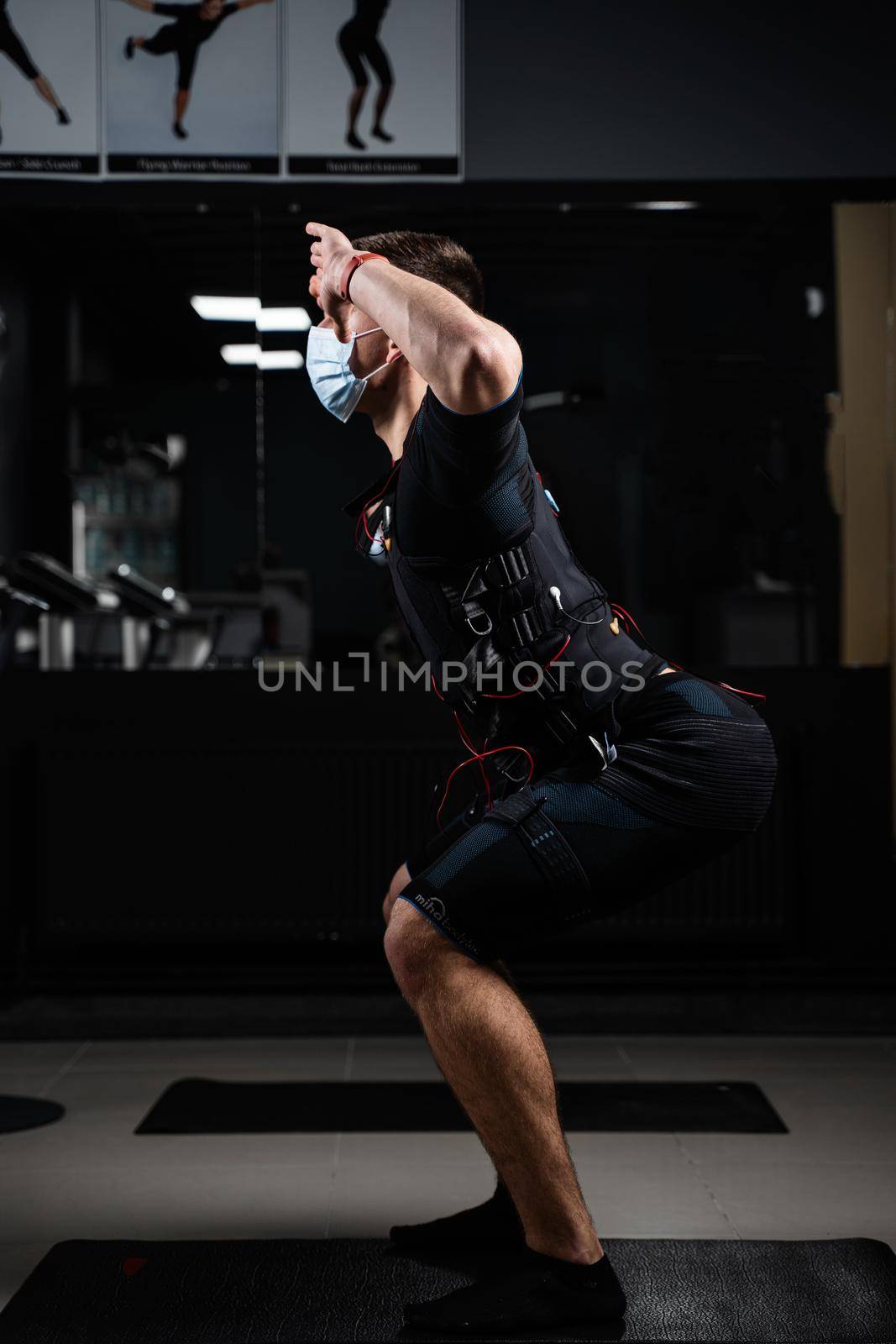 Man in EMS suit and medical mask in gym. Protection from coronavirus covid-19. Sport training in electrical muscle stimulation suit at quarantine period