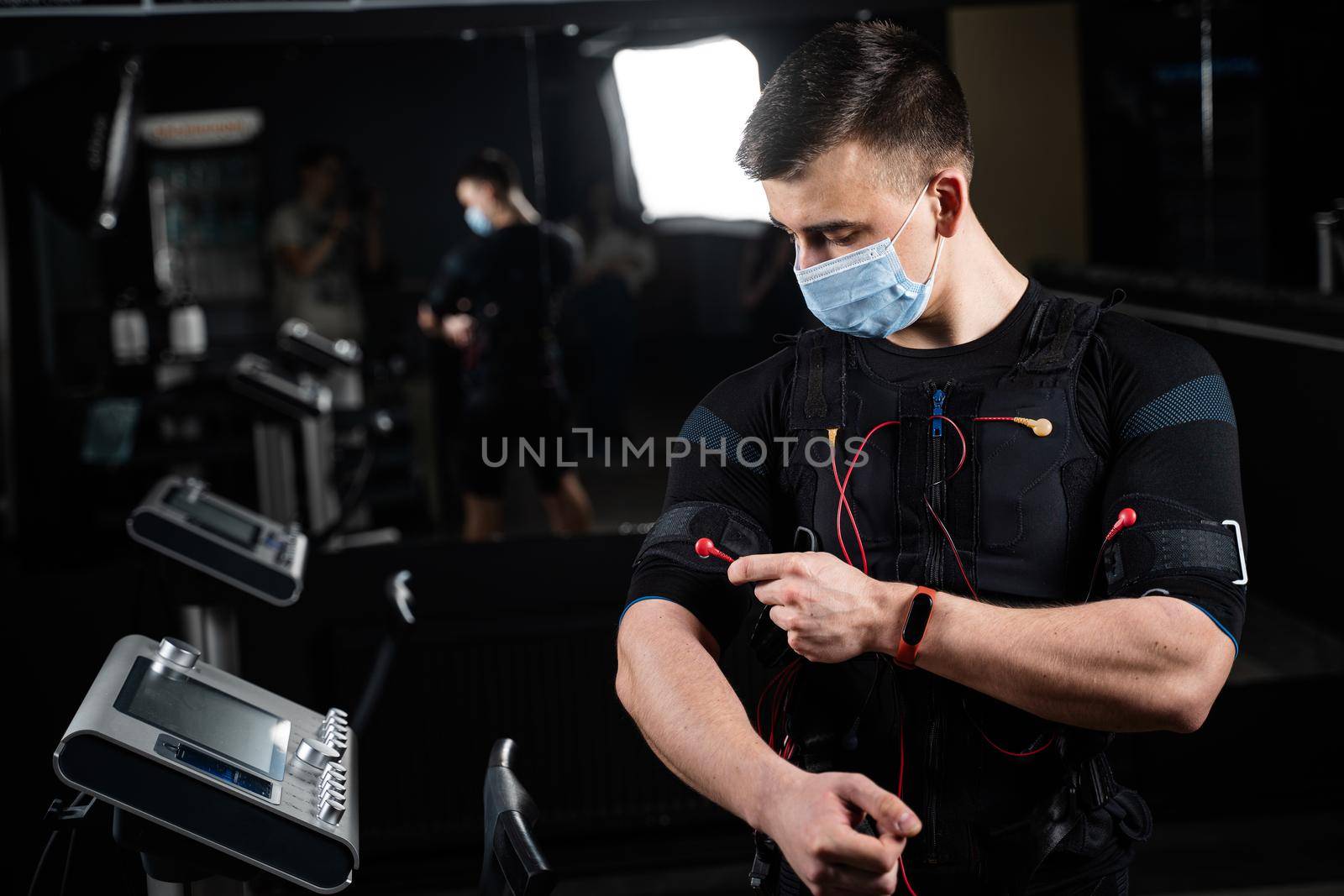 Man in EMS suit and medical mask in gym. Protection from coronavirus covid-19. Sport training in electrical muscle stimulation suit at quarantine period