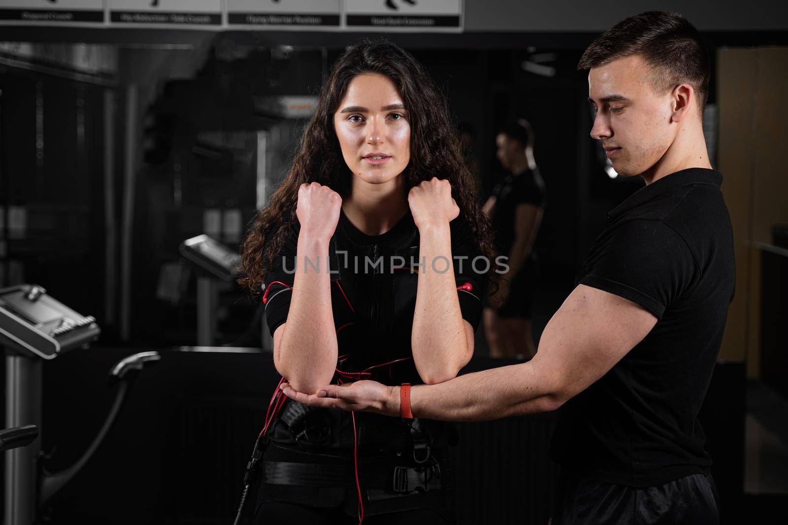 Man trainer trains a girl in an EMS suit in the gym. Electrical stimulation of the misc during active training.