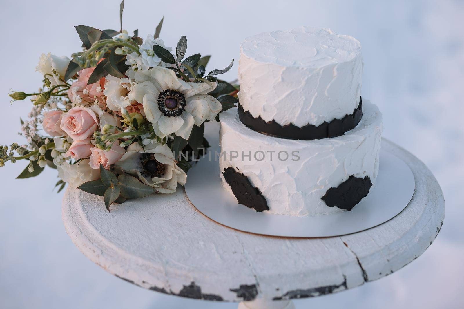 A cake in black and white design, standing on a stand in a winter forest on the snow. There is a wedding bouquet nearby by deandy