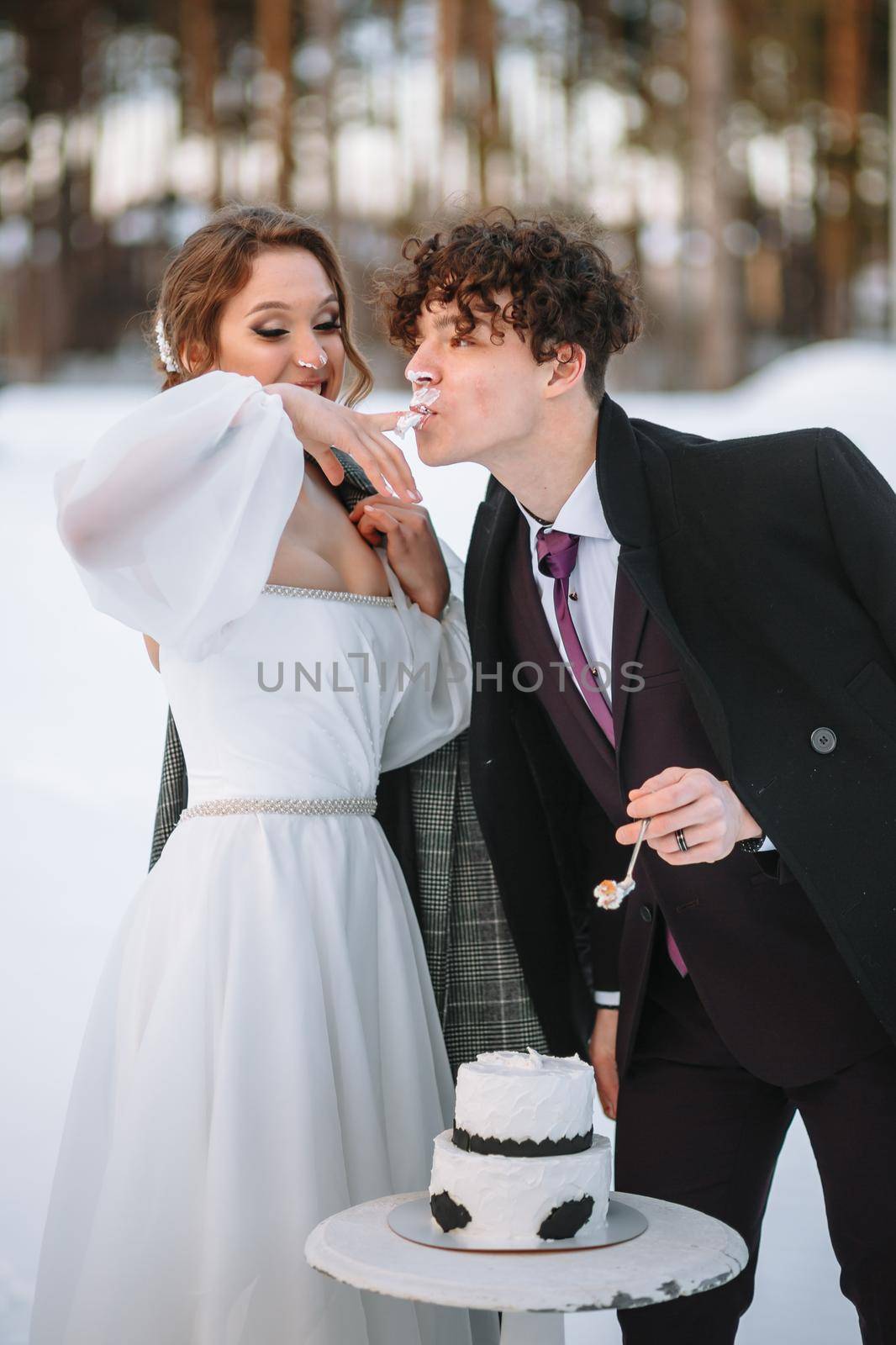 The groom licks the remains of the wedding cake from the bride's finger. Shooting in the winter forest by deandy
