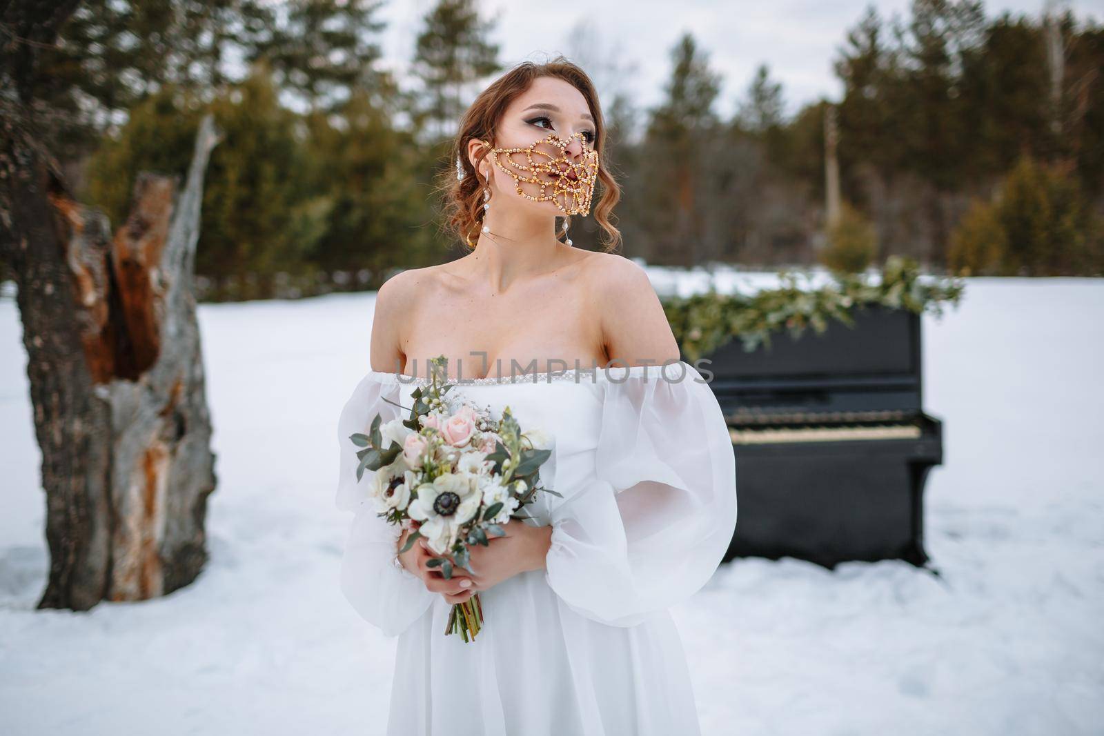 The bride is standing in a snow-covered forest. The bride is wearing a fabulous protective mask.