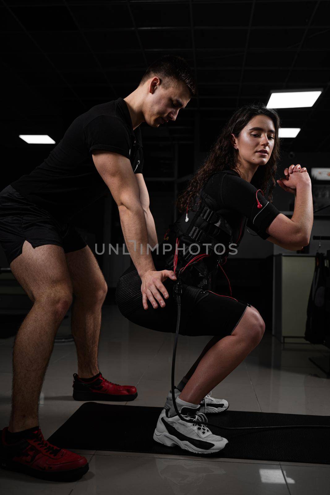 Man trainer trains a girl in an EMS suit in the gym. Electrical stimulation of the misc during active training by Rabizo