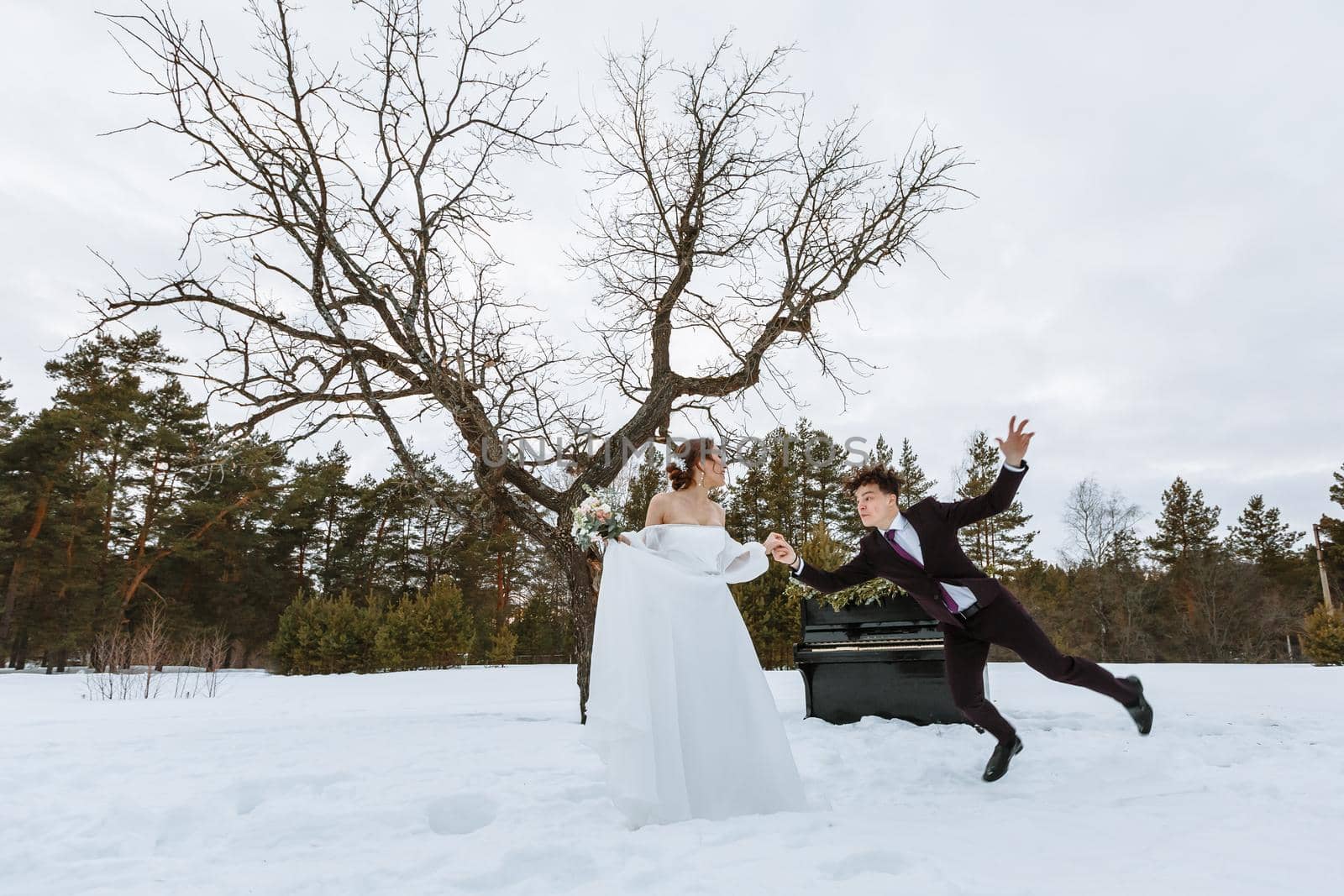 The bride holds the groom's hand. Winter forest, with a piano in the background. The groom slipped by deandy