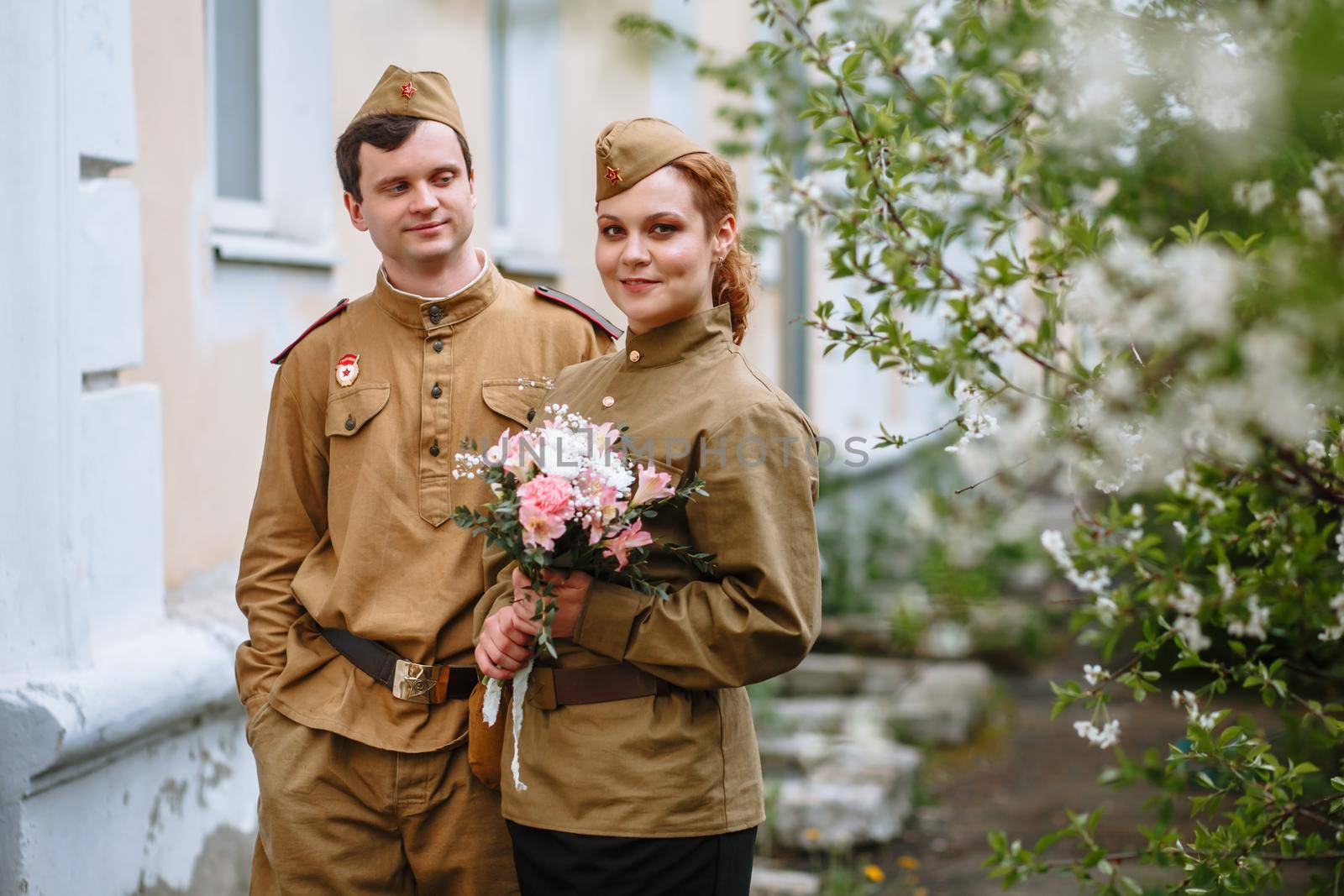 People in Soviet military uniforms. A couple stands by a tree by deandy