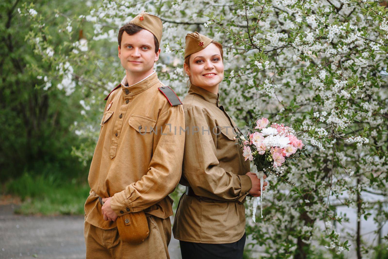 Portrait of two military lovers at a flowering tree. Warm spring, people are returning from the war