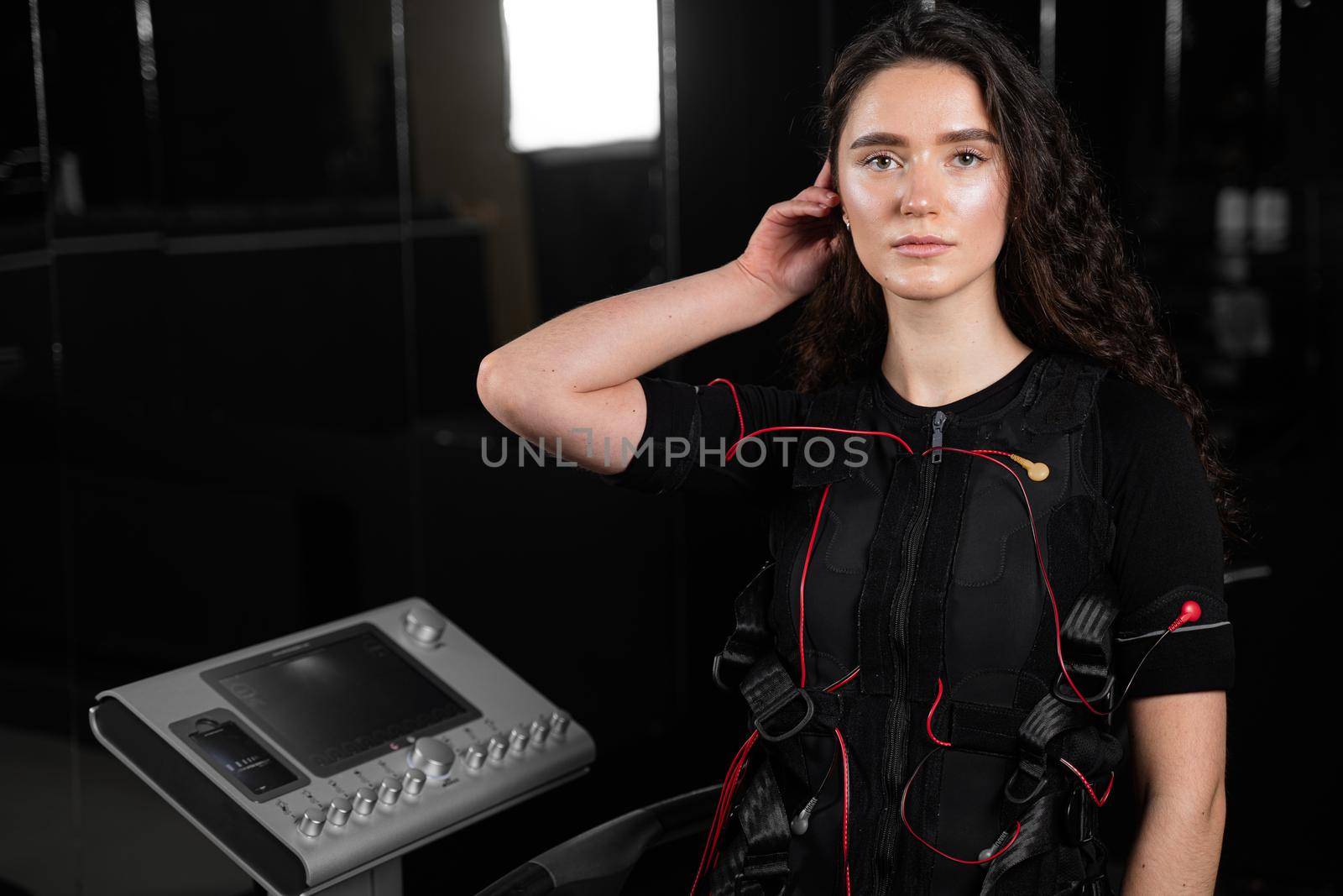 Girl in EMS suit in gym. Sport training in electrical muscle stimulation suit. Making physical exercises.