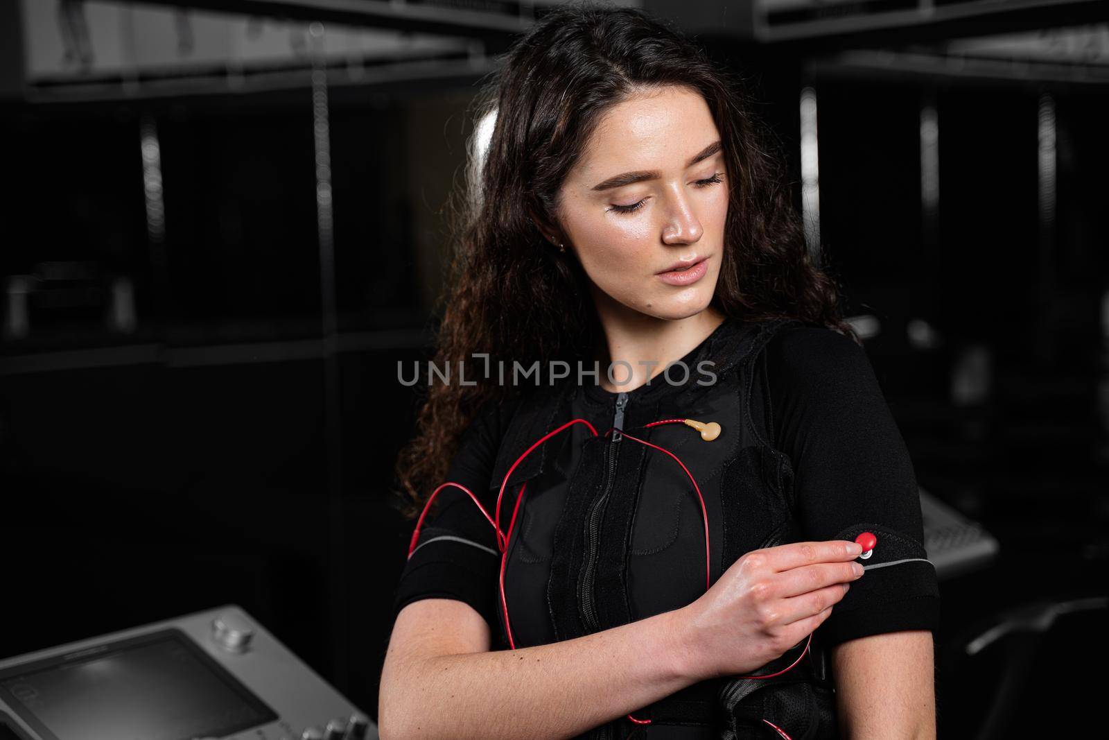 Girl in EMS suit in gym. Sport training in electrical muscle stimulation suit. Making physical exercises.