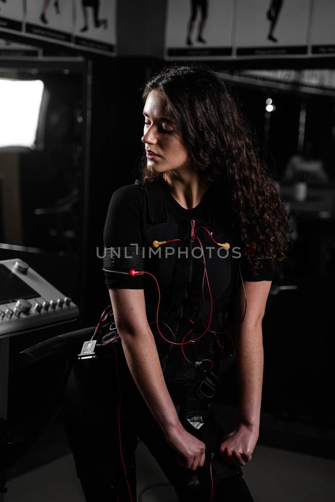 Girl in EMS suit in gym. Sport training in electrical muscle stimulation suit. Making physical exercises by Rabizo