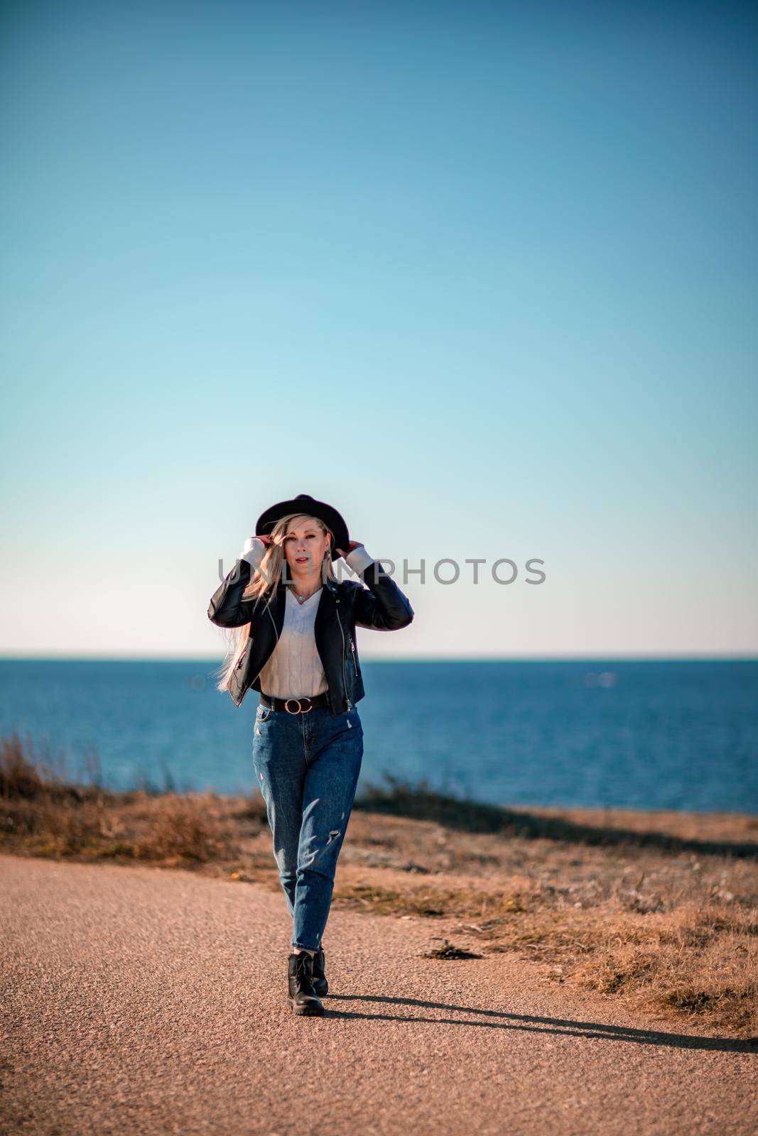 A blonde in a stylish black leather jacket walks along the seashore