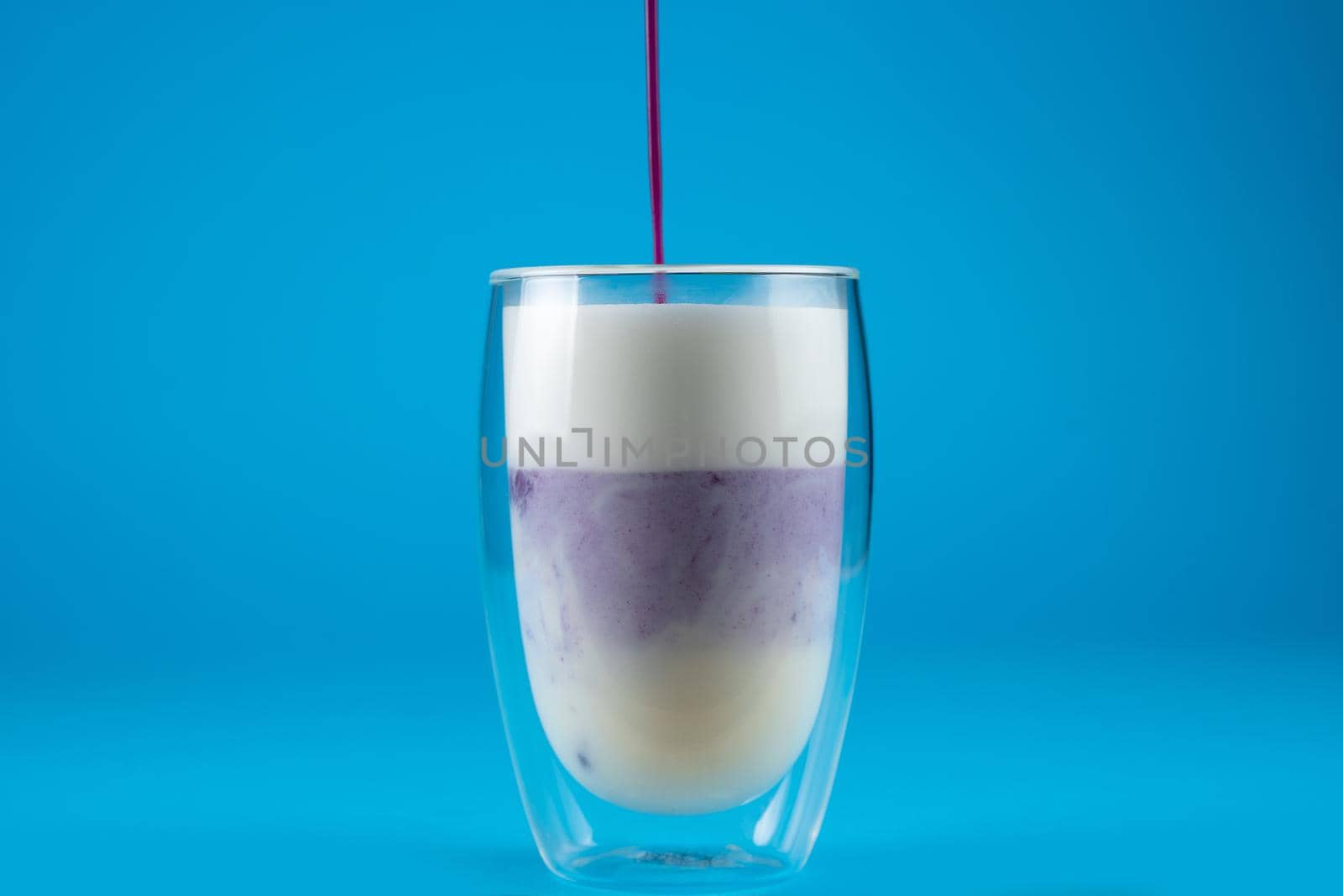 Pouring purple goji matcha in double glass cup. Matcha cocktail on blue background