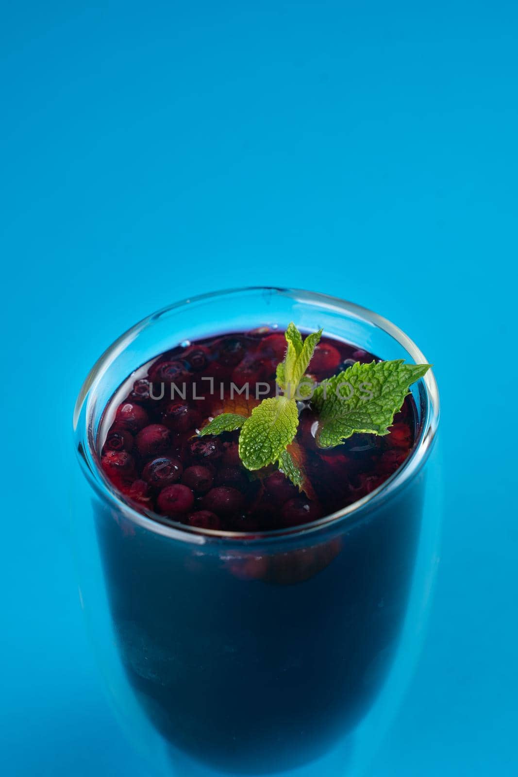 Blueberry tea in double glass cup on blue background.