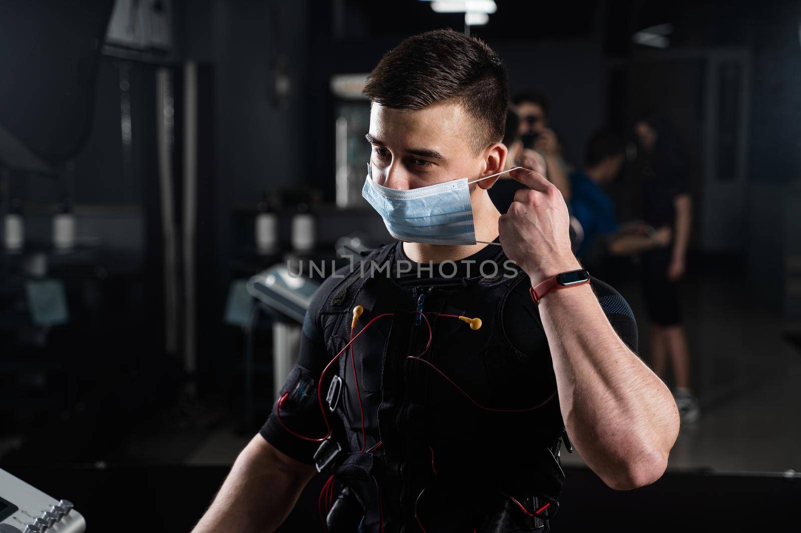 Man in EMS suit and medical mask in gym. Protection from coronavirus covid-19. Sport training in electrical muscle stimulation suit at quarantine period. by Rabizo