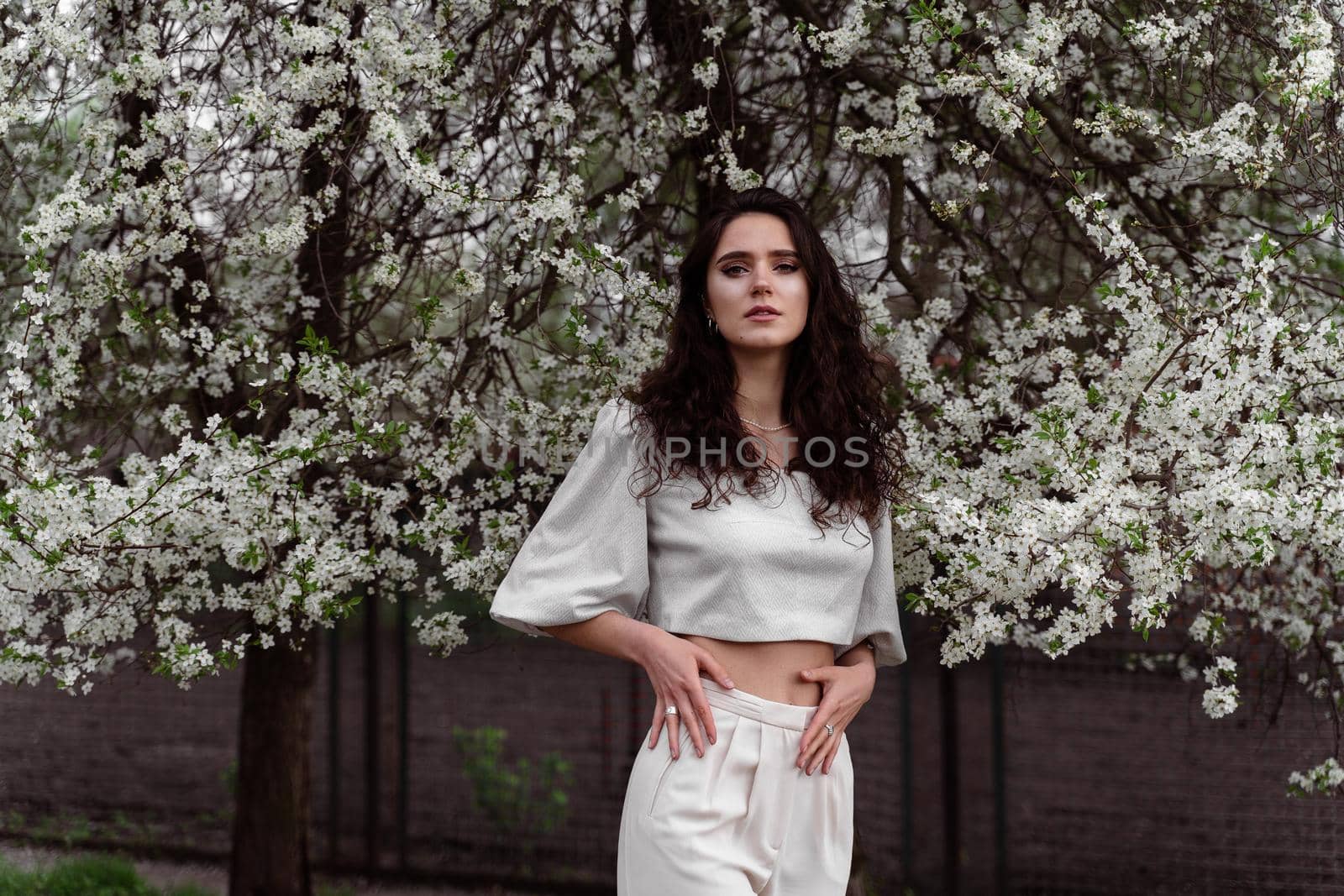 Portrait of young woman in the garden. Attractive girl weared white dress posing near blooming trees