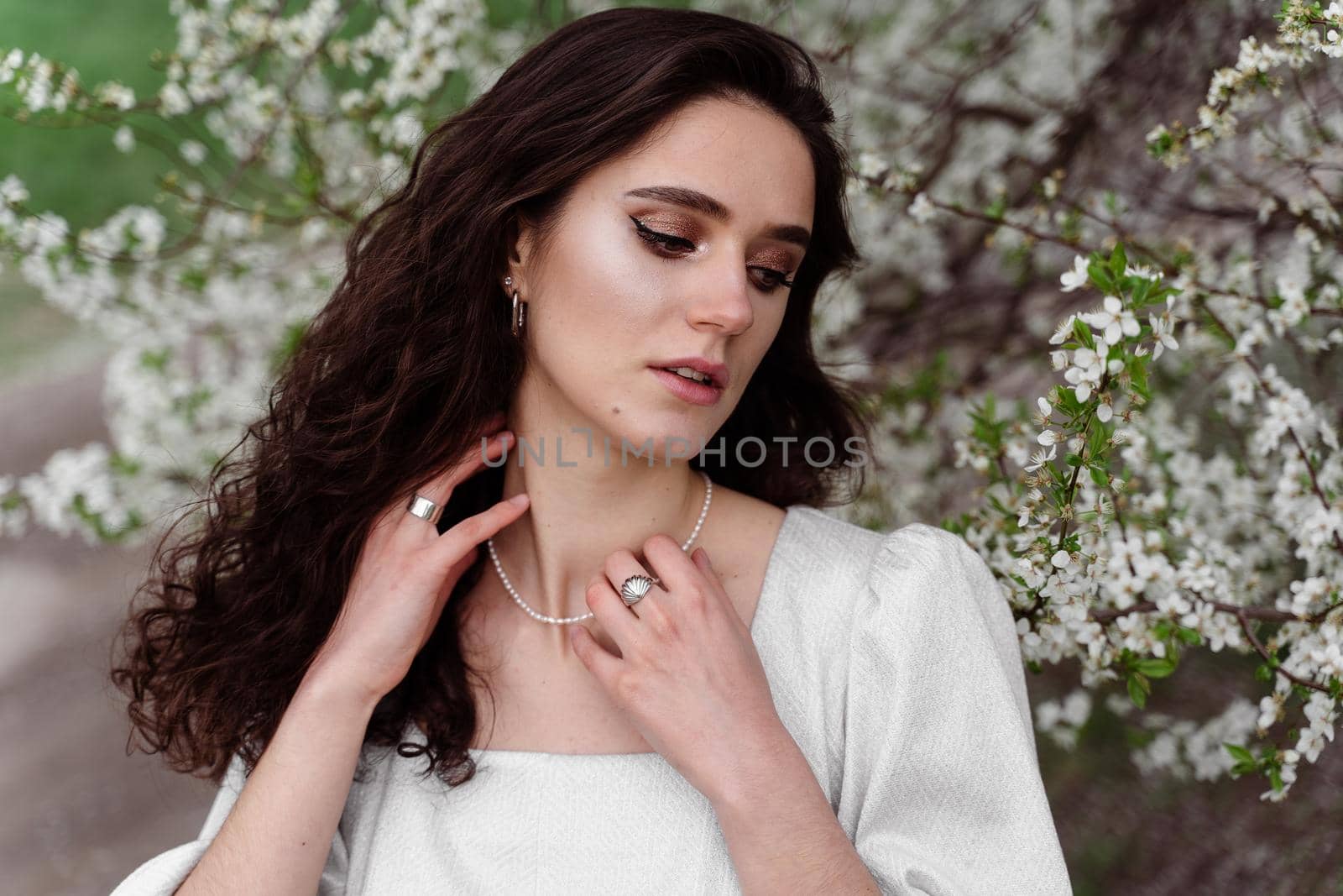 Spring lifestyle. Model posing near white blooming trees without mask outdoor countryside. Dreaming girl with curly hair